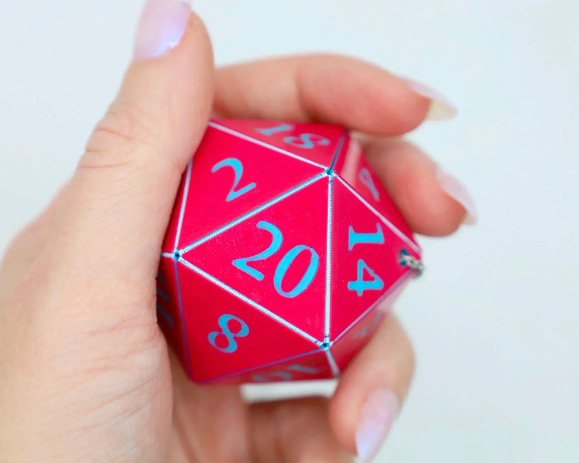 Hand holding a large red twenty-sided dice with blue numbers, tabletop RPG accessory.