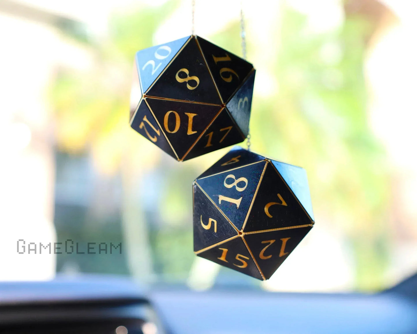 Black twenty-sided dice car charms with gold numbers hanging in a car interior