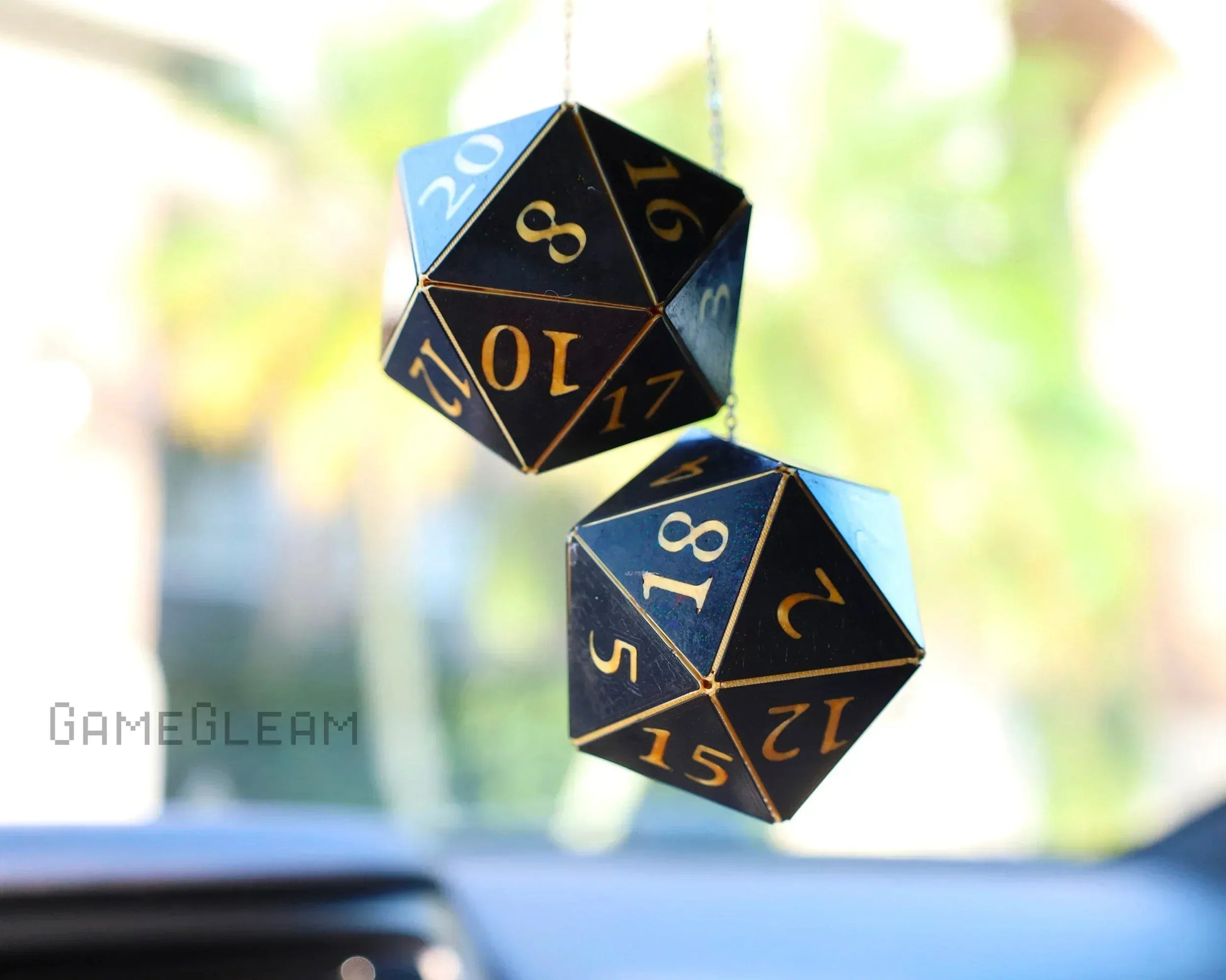 Black twenty-sided dice car charms with gold numbers hanging in a car interior