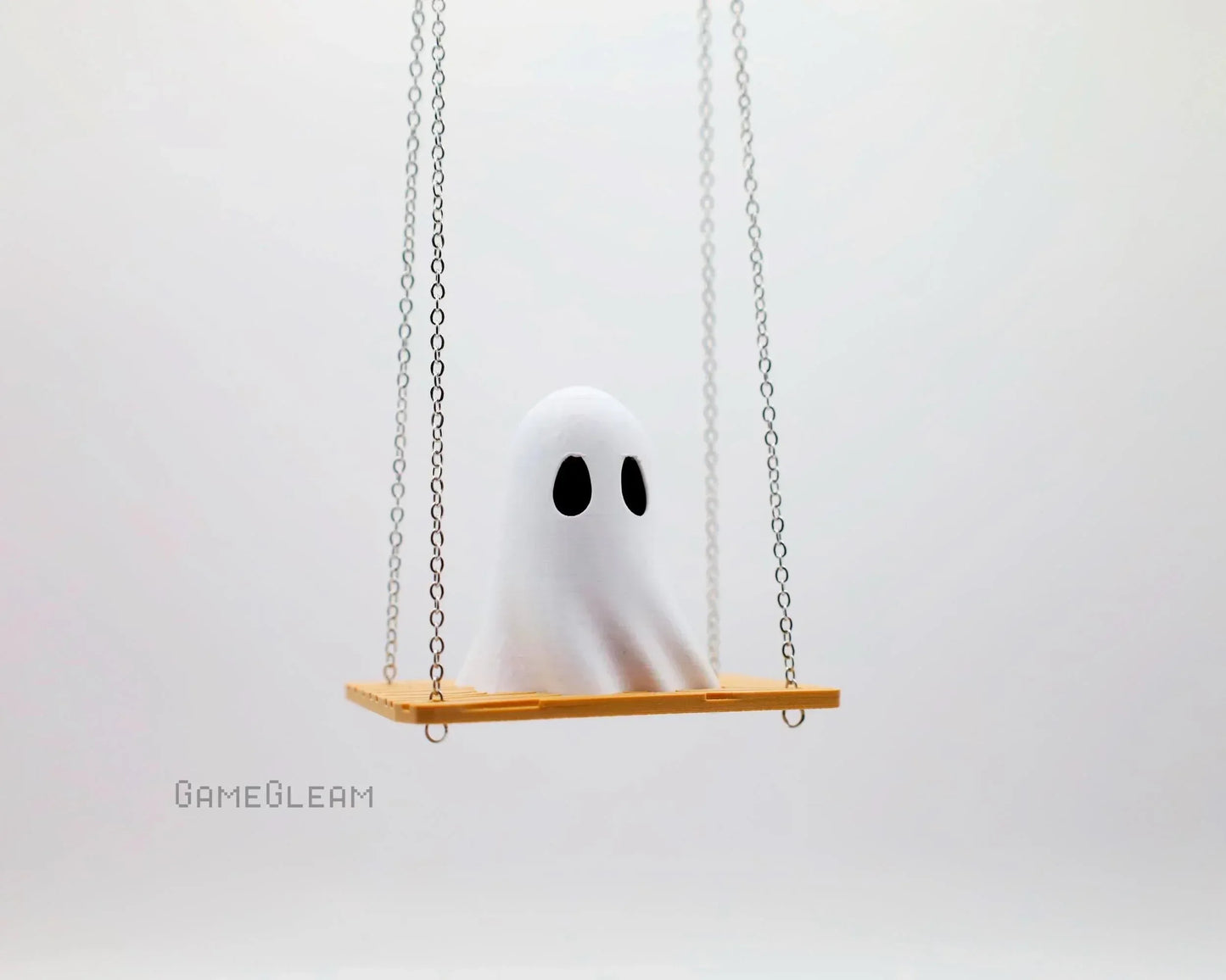 Cute handmade white ghost figure with black eyes sitting on a small swing with chains