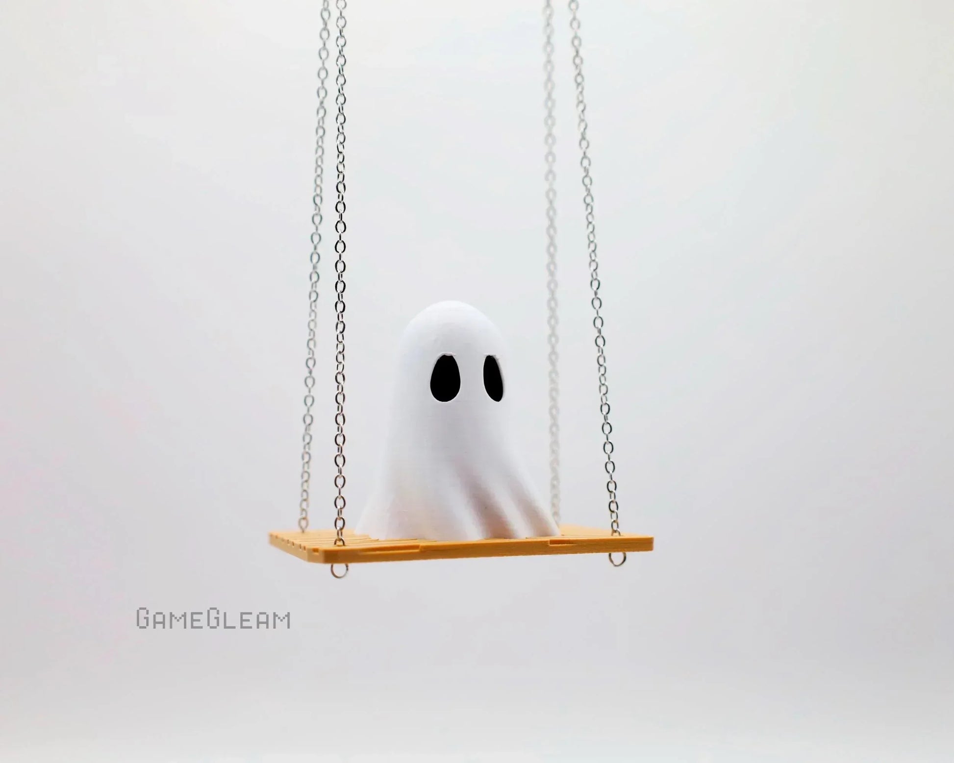 Cute handmade white ghost figure with black eyes sitting on a small swing with chains