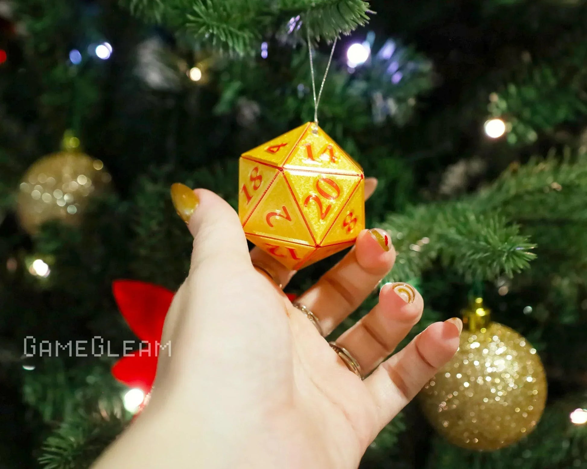 Hand holding a glittery orange twenty-sided dice ornament on a Christmas tree with gold baubles