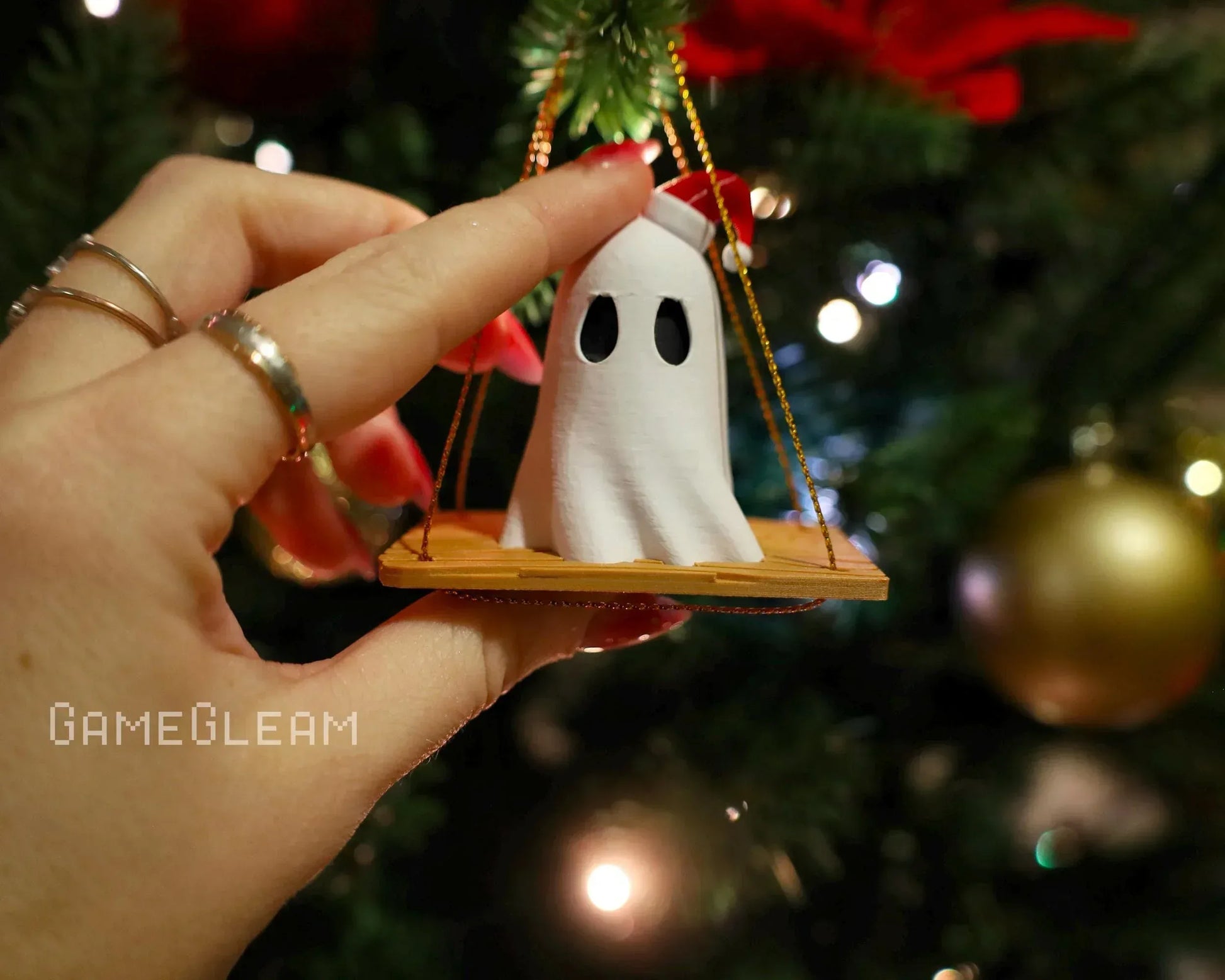 Hand holding cute ghost Christmas ornament with Santa hat on swing, Christmas tree background