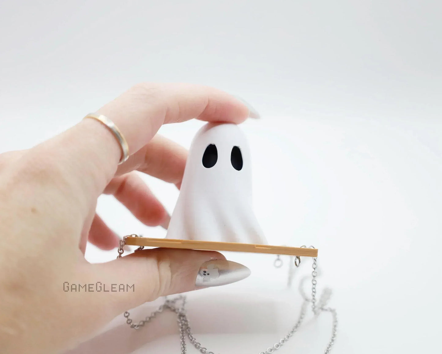 Hand holding a cute handmade ghost charm with black eyes and a long silver chain.