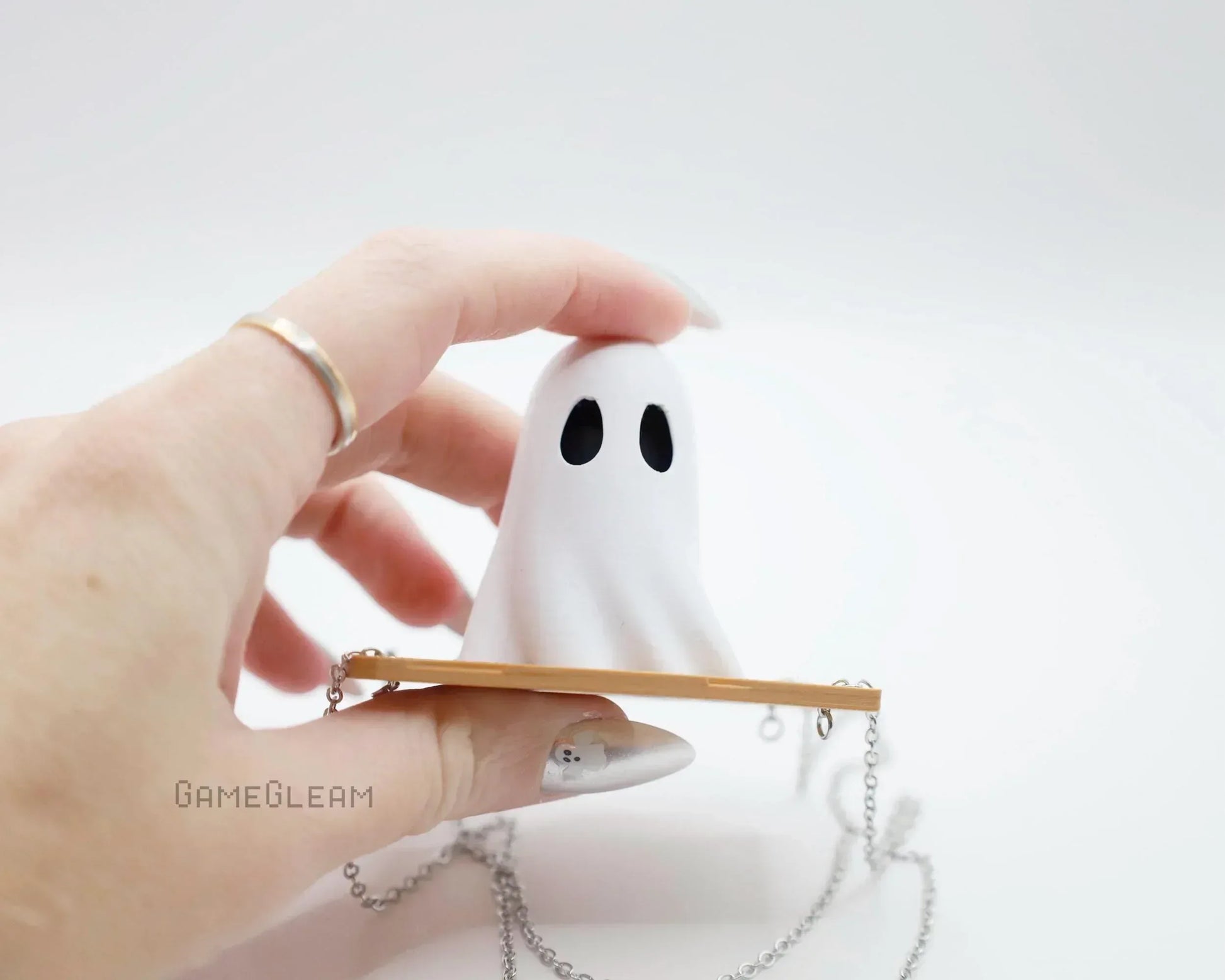 Hand holding a cute handmade ghost charm with black eyes and a long silver chain.