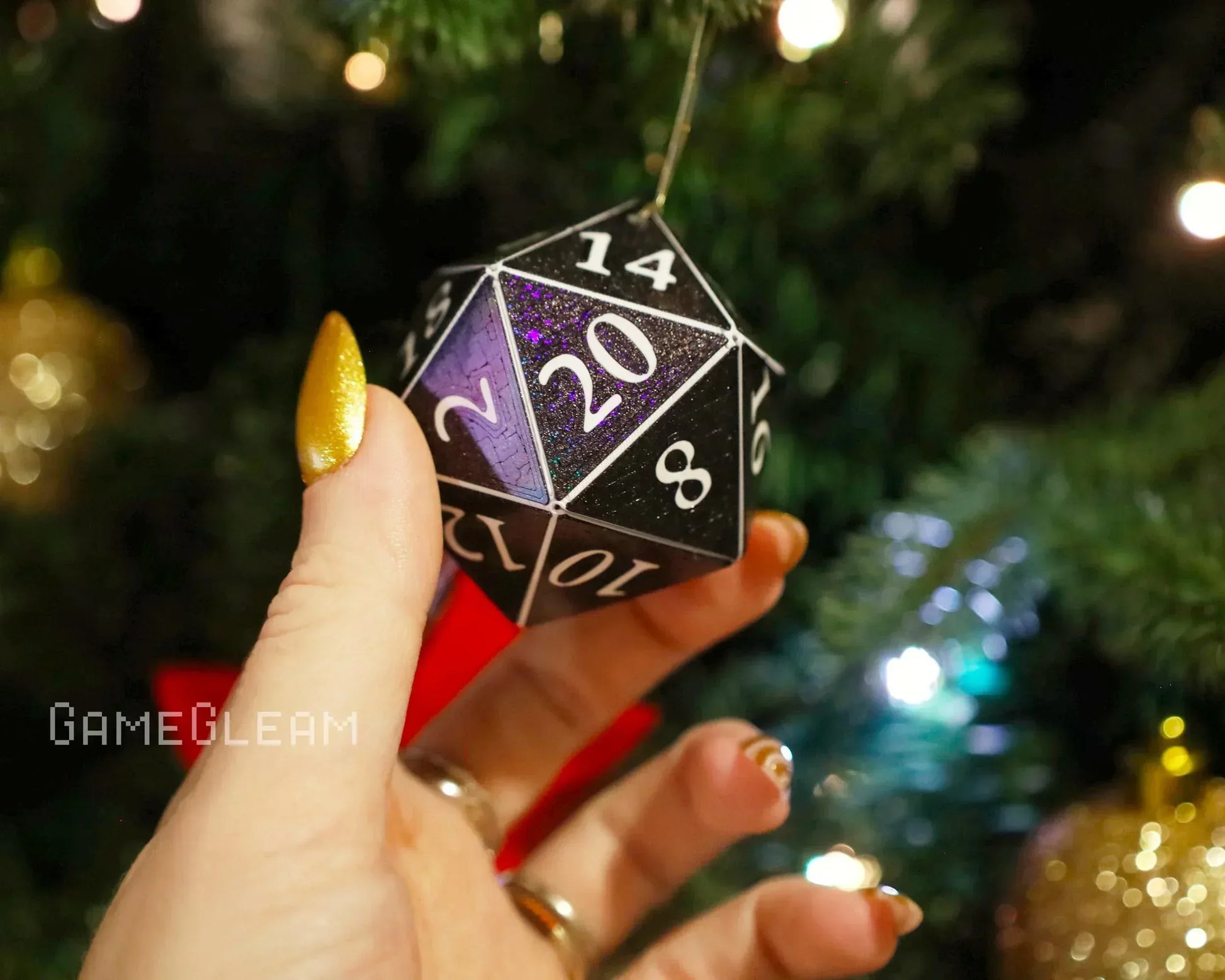 Hand holding a holographic black twenty-sided dice ornament near a Christmas tree