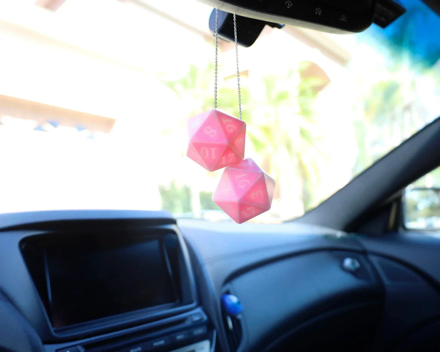 Pink twenty-sided dice hanging as car mirror charm in a bright car interior