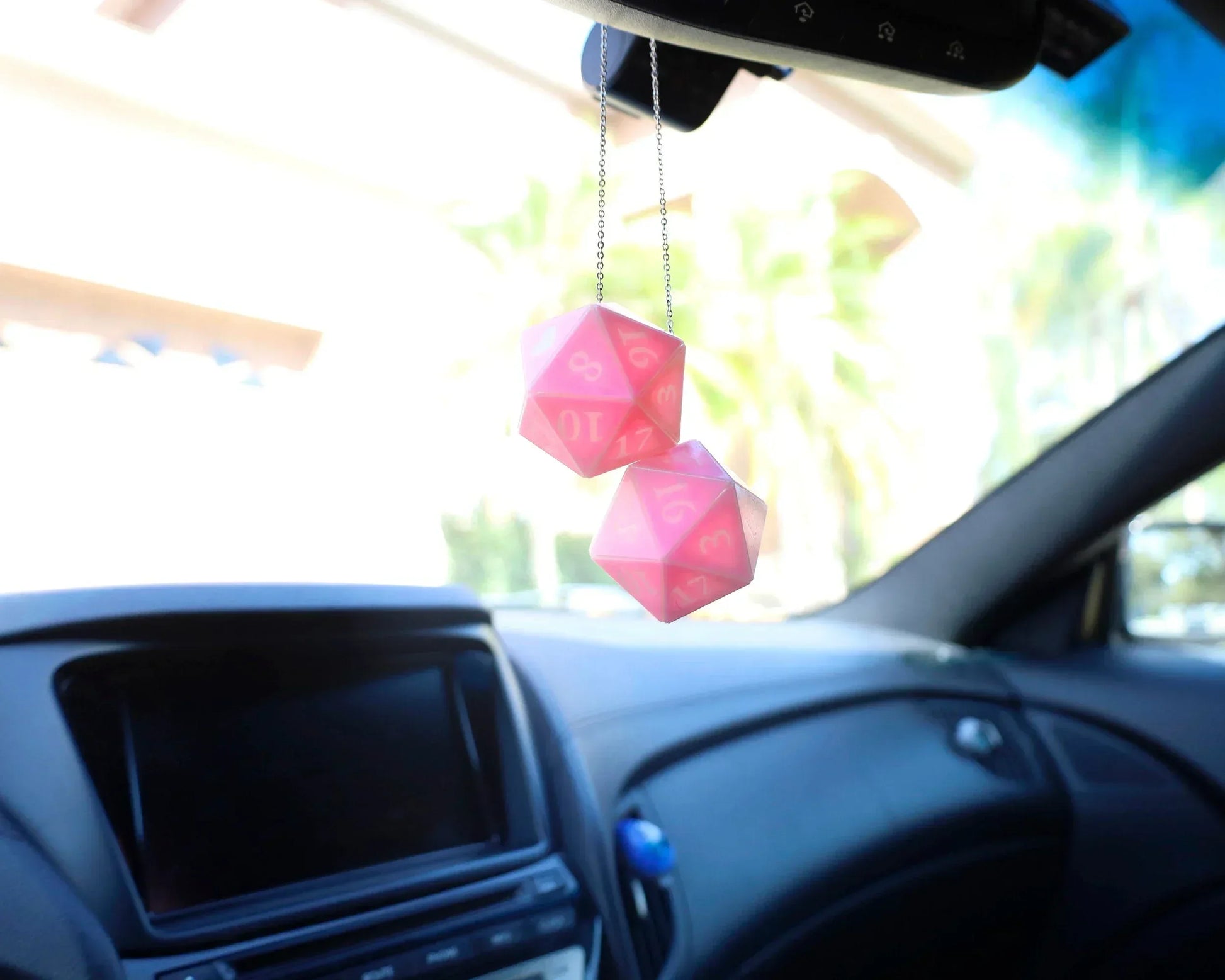 Pink twenty-sided dice hanging as car mirror charm in a bright car interior
