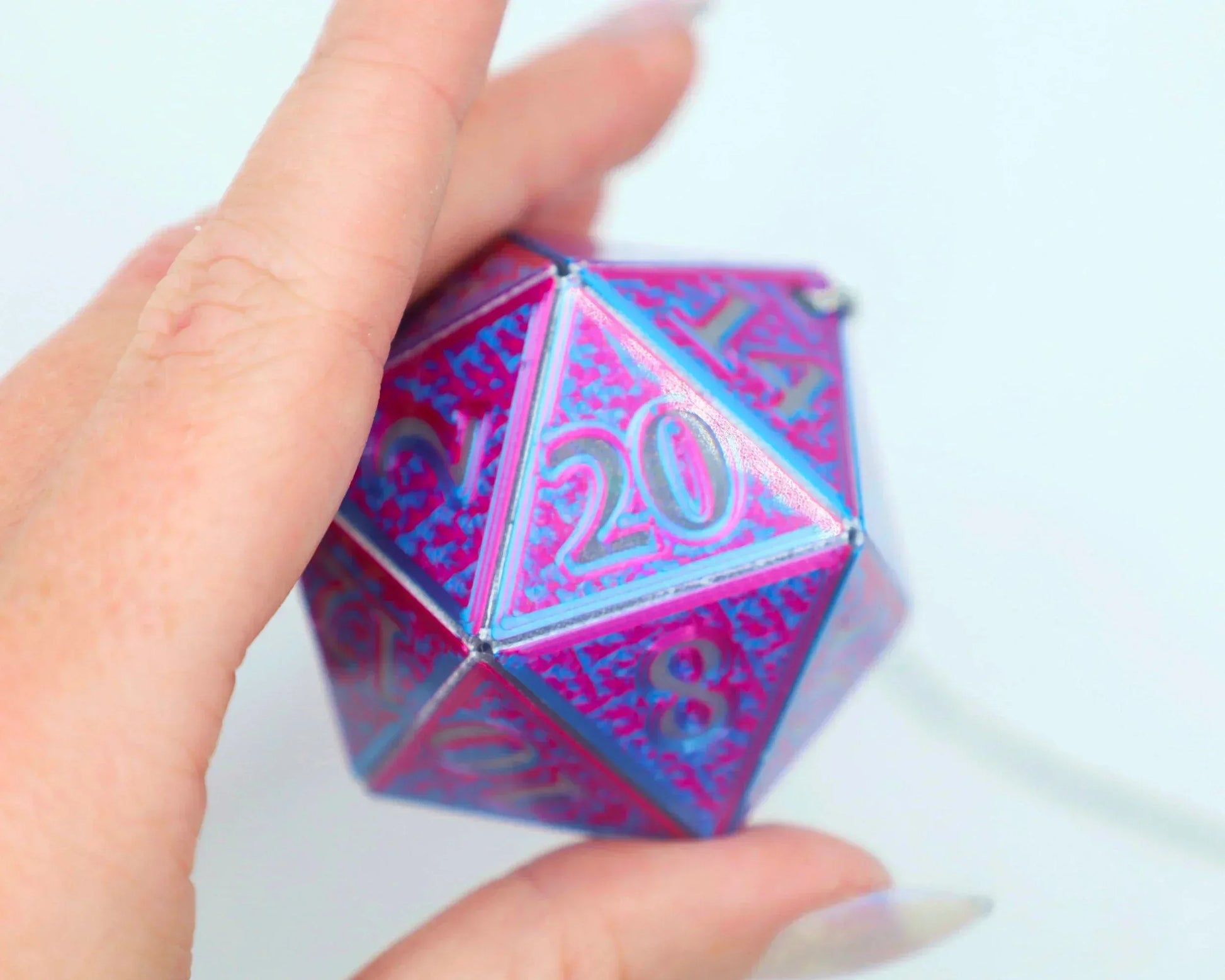 Hand holding a large holographic pink and blue twenty-sided dice charm