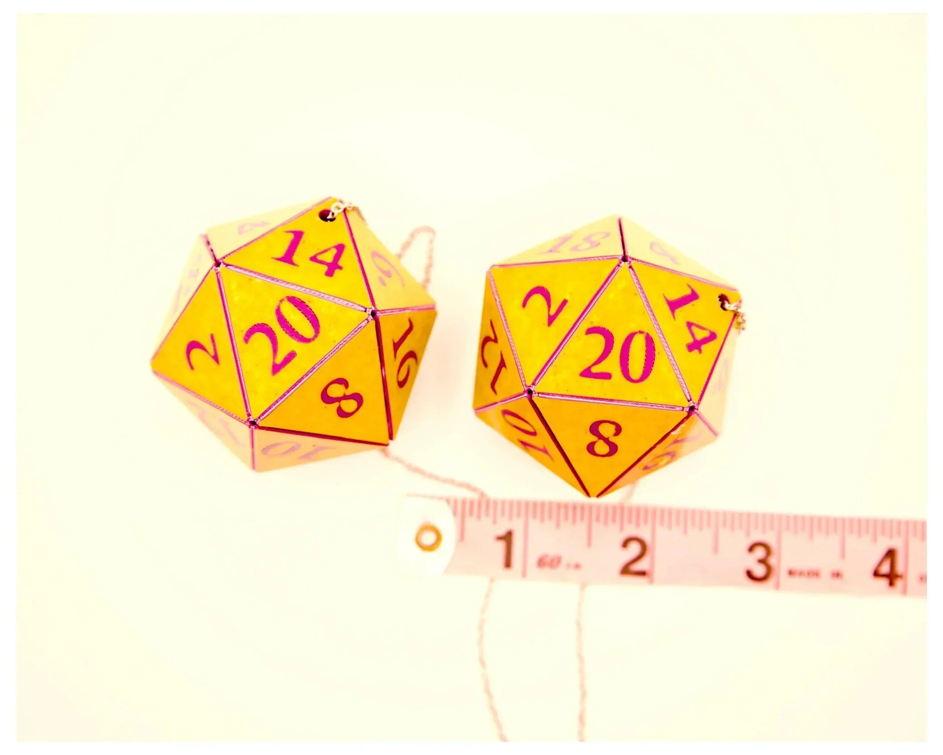 Yellow twenty-sided dice car charms with pink numbers next to a measuring tape