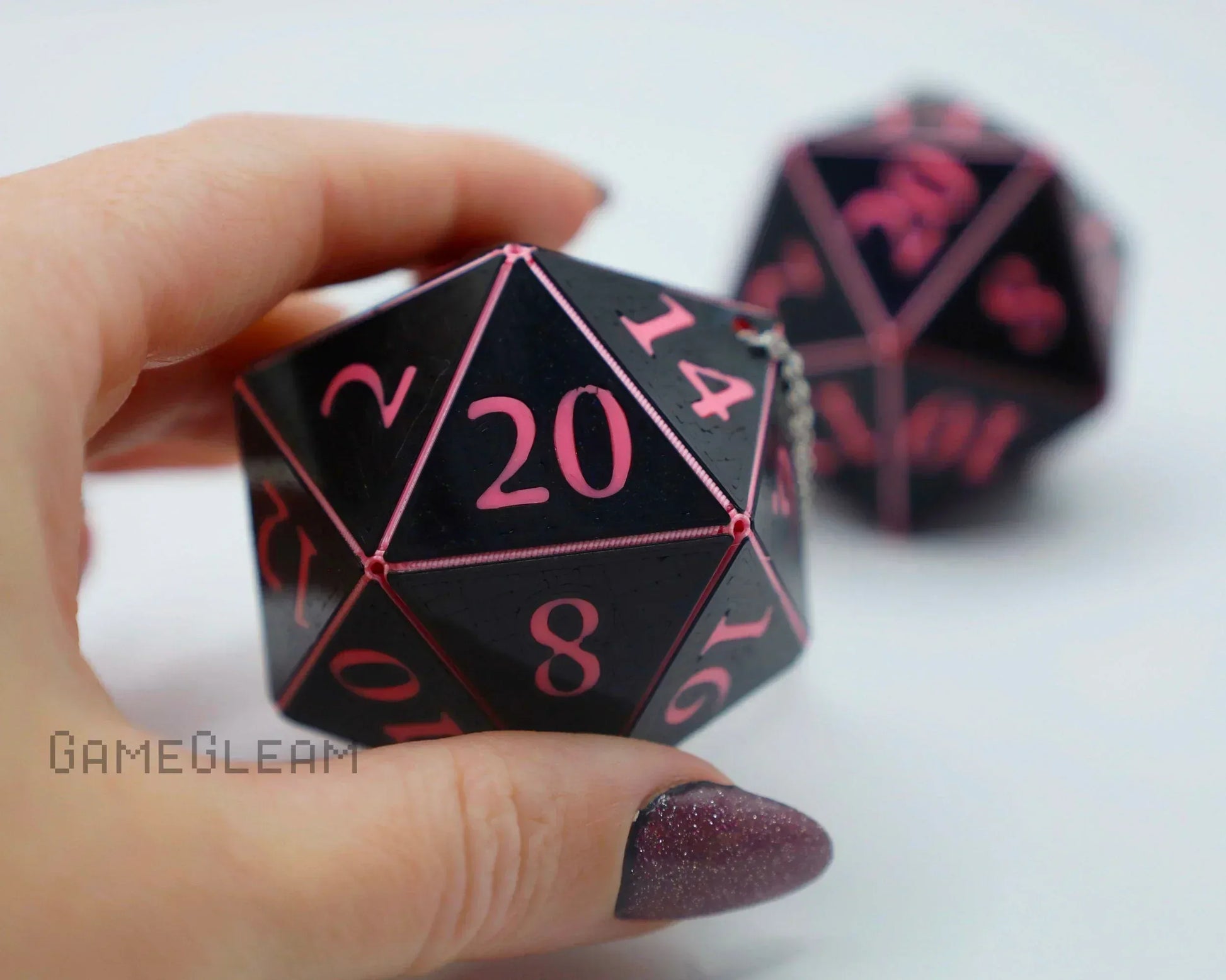 Hand holding a black and pink 20-sided resin dice charm for tabletop gaming or car accessory.