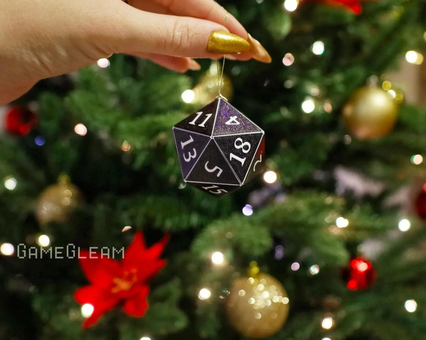 Hand holding black 20-sided dice ornament in front of Christmas tree with festive lights