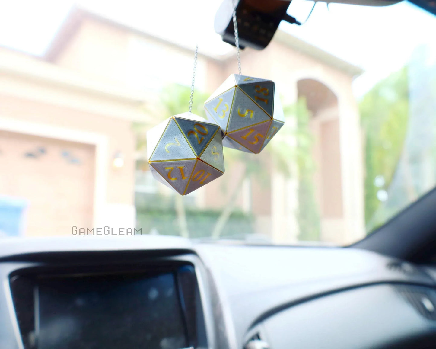 Pair of gray and gold twenty-sided dice car charms hanging from rearview mirror