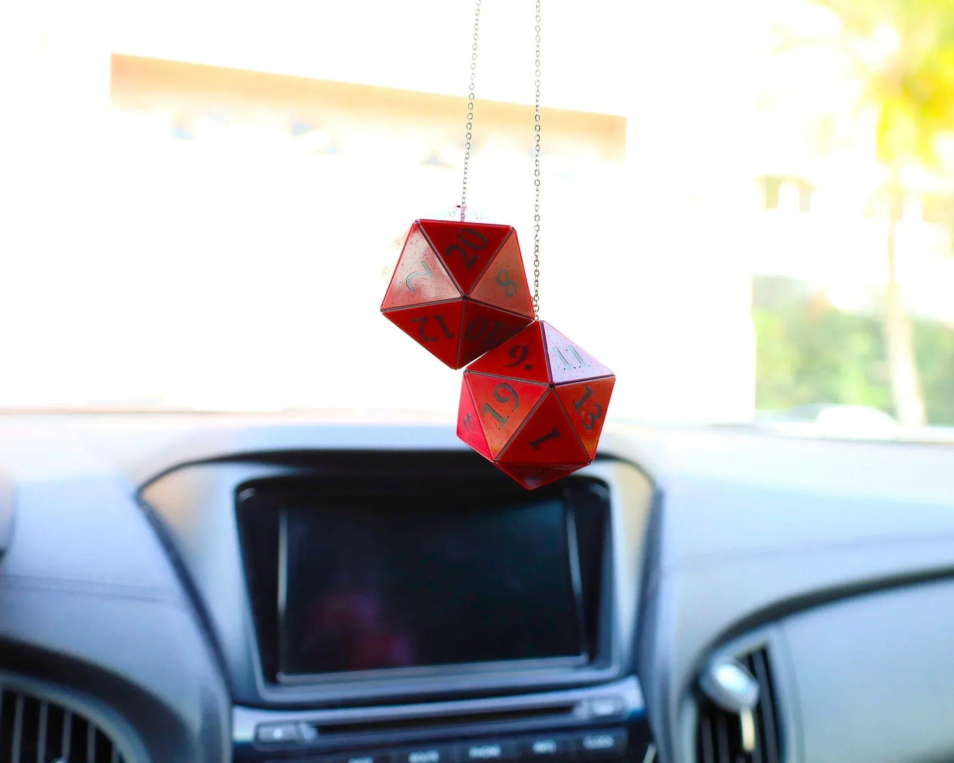 Red twenty-sided dice car charm hanging from rearview mirror in car interior