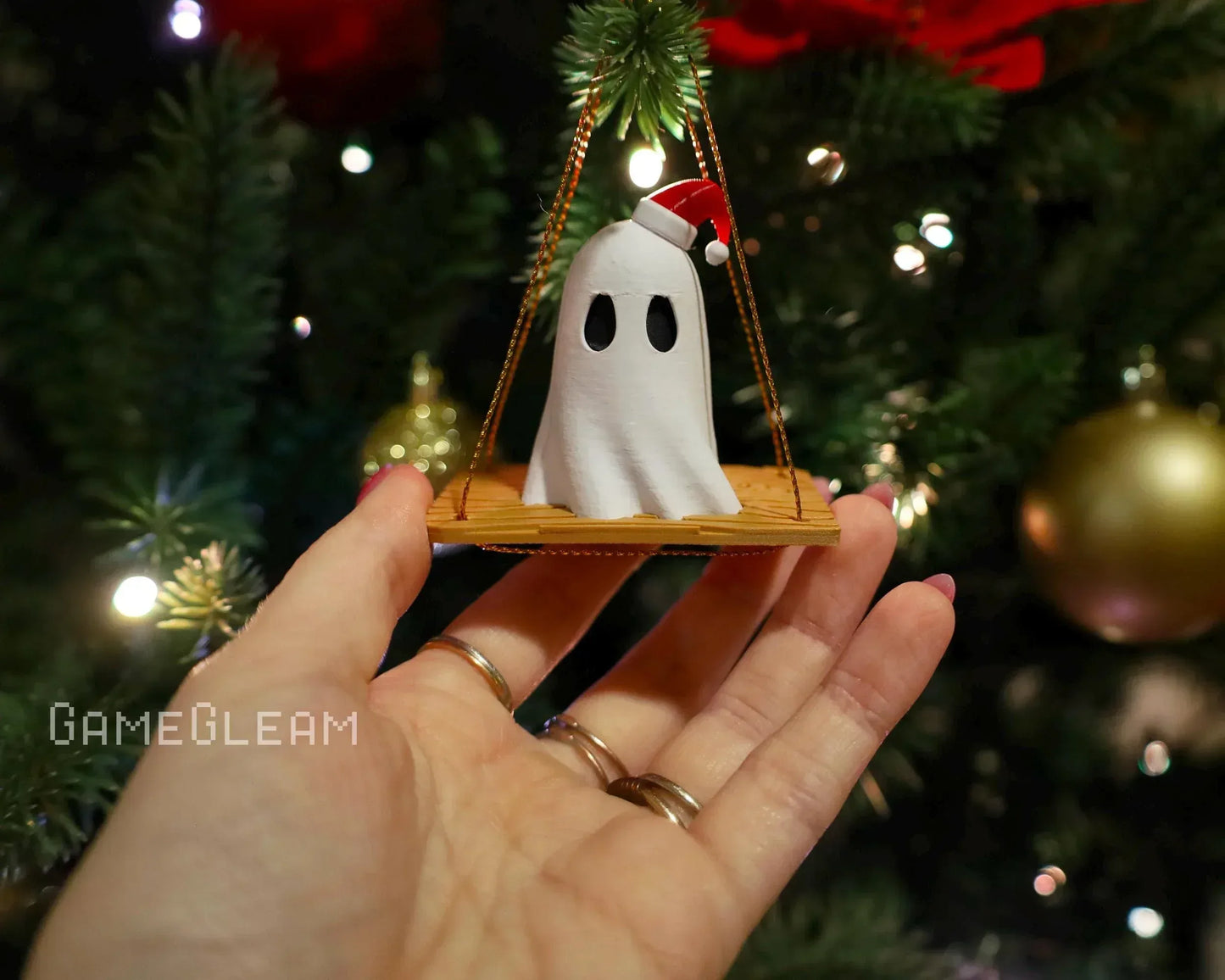 Hand holding a handmade ghost ornament with Santa hat, Christmas tree in background