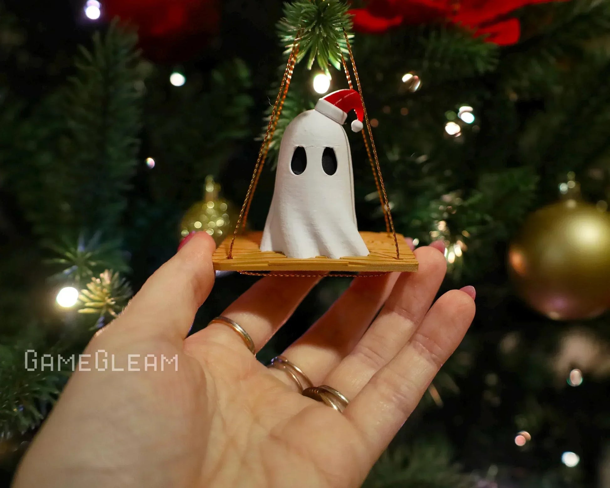 Hand holding a handmade ghost ornament with Santa hat, Christmas tree in background