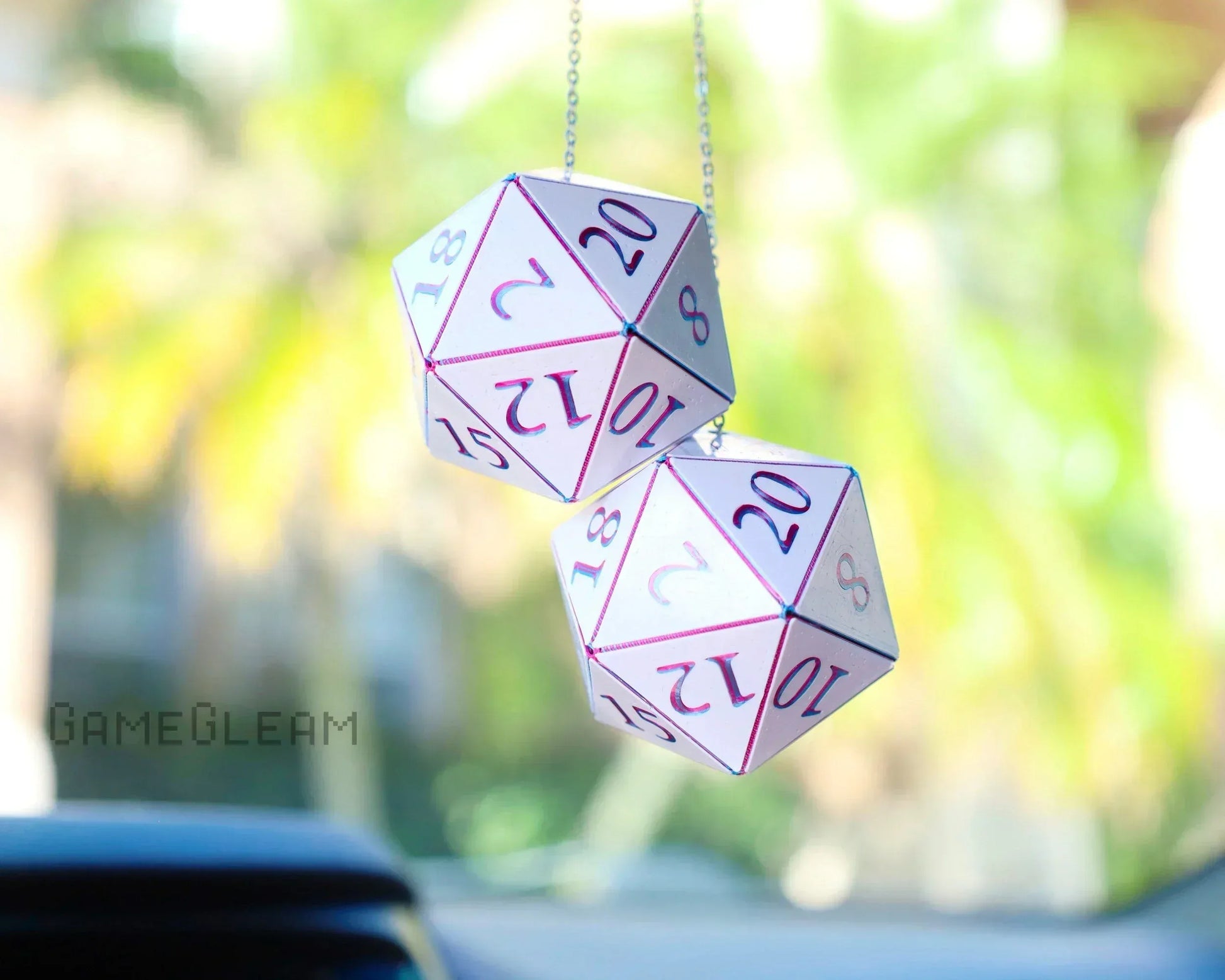 Holographic pink double twenty-sided dice hanging as car mirror charm, sunlight background.