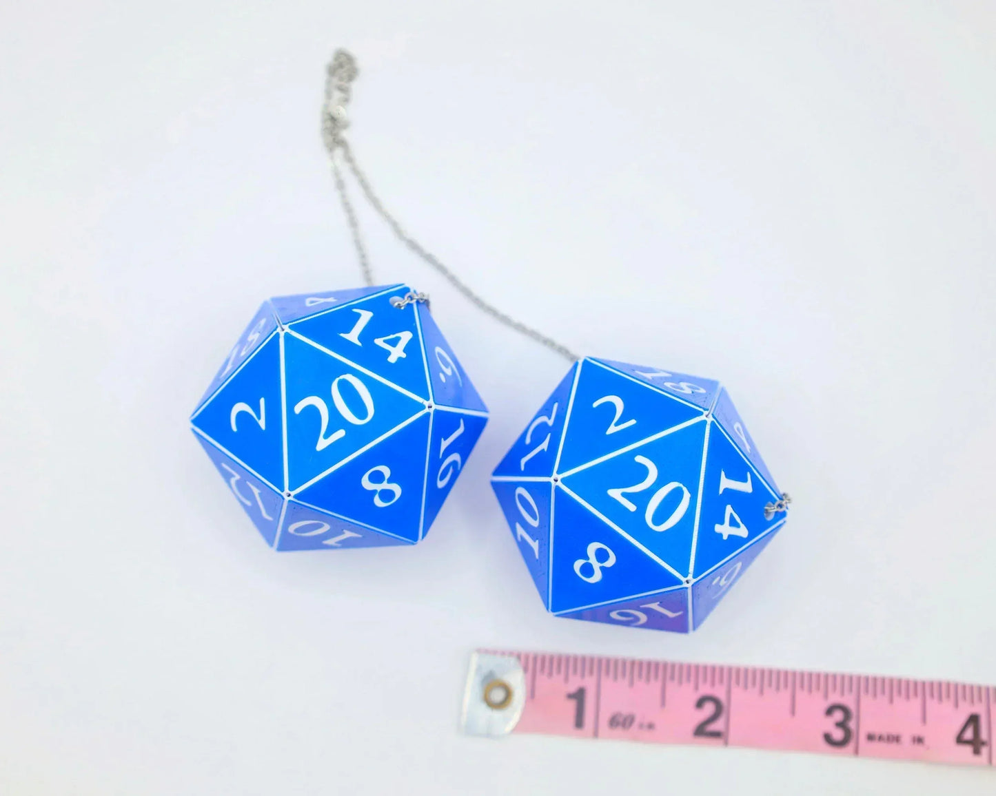 Blue 20-sided dice car charm with chain, shown next to a pink measuring tape