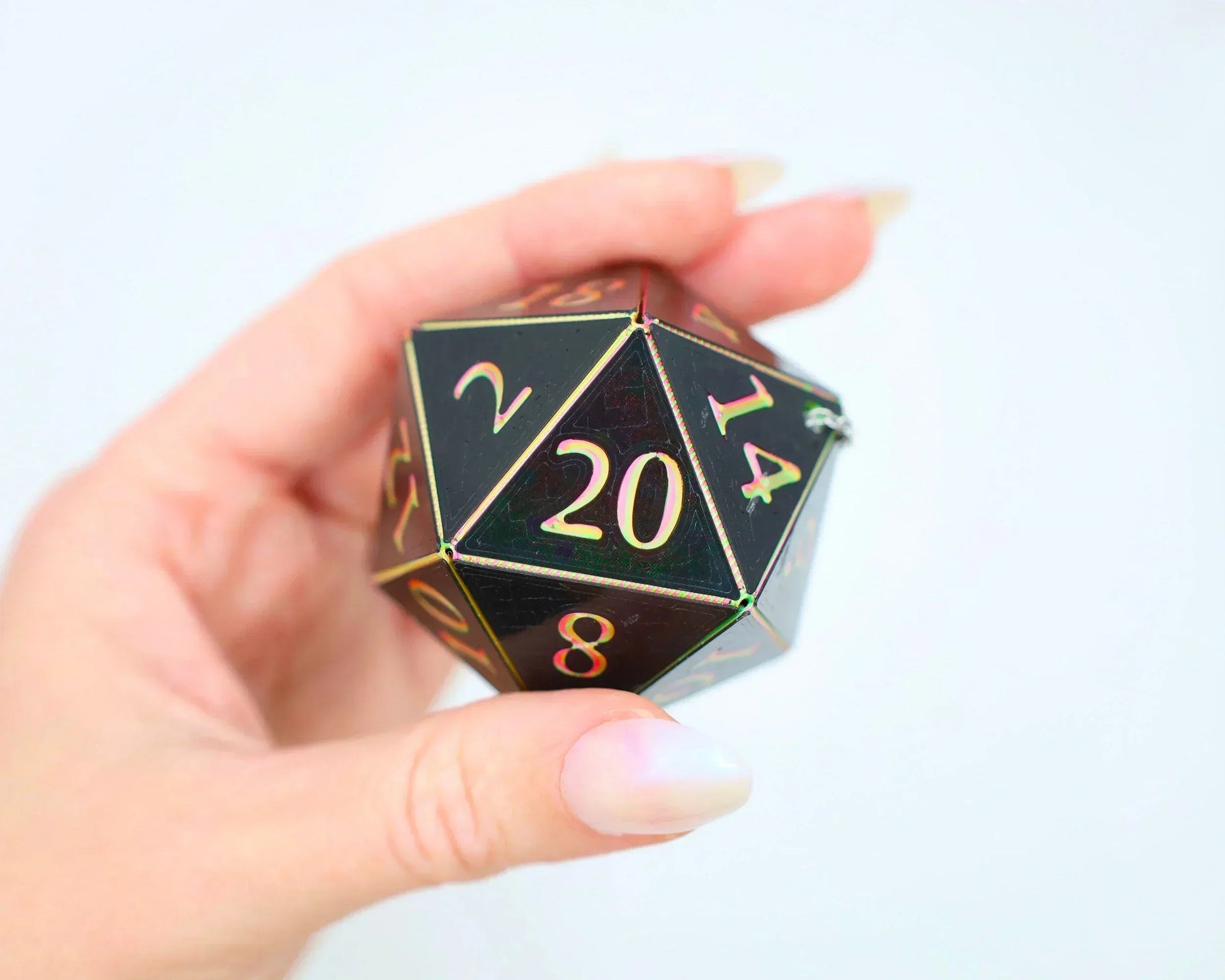 Hand holding holographic black 20-sided dice charm with gold numbers for tabletop RPG gaming
