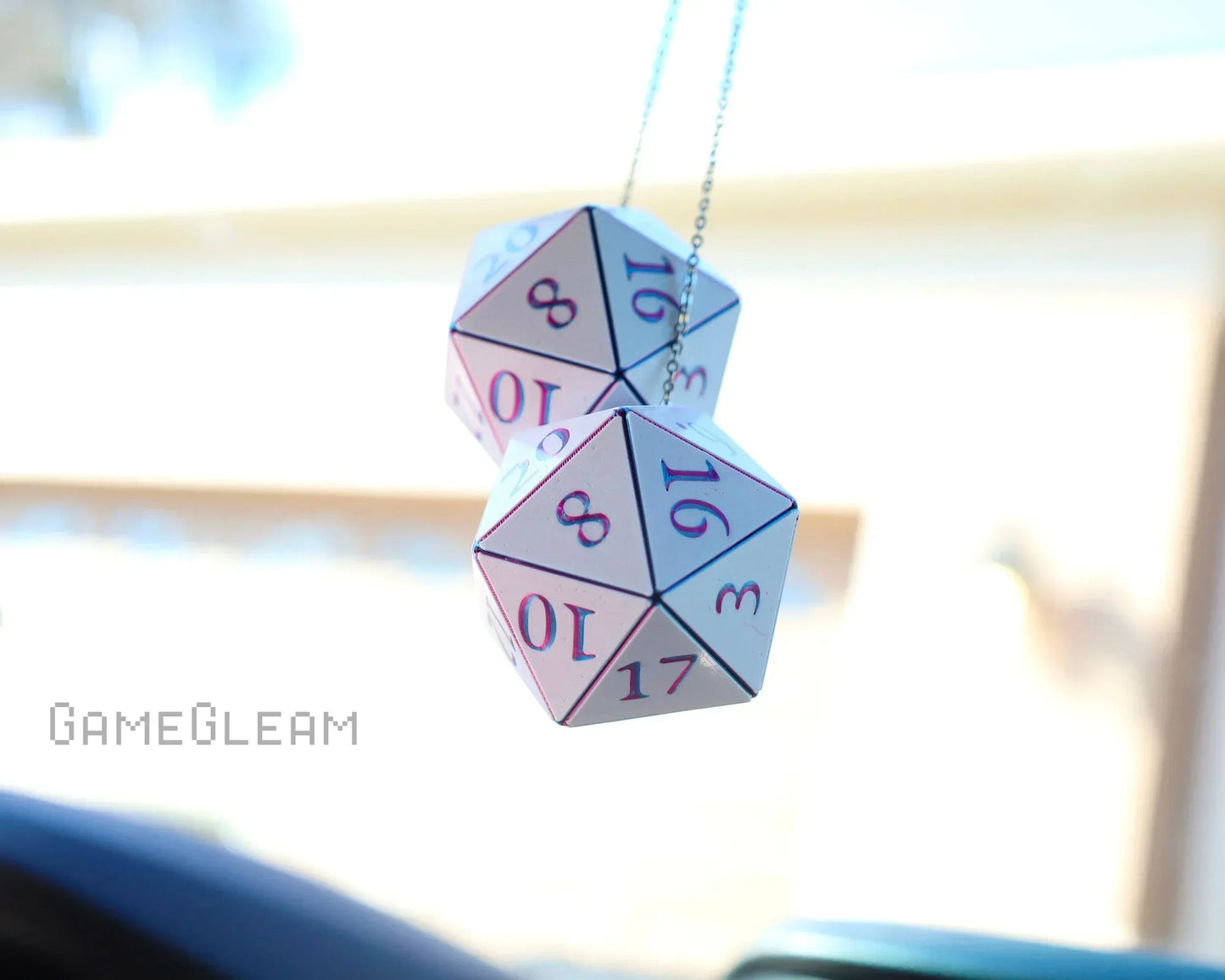 Pair of holographic 20-sided dice car charms hanging on chains, sunlit background