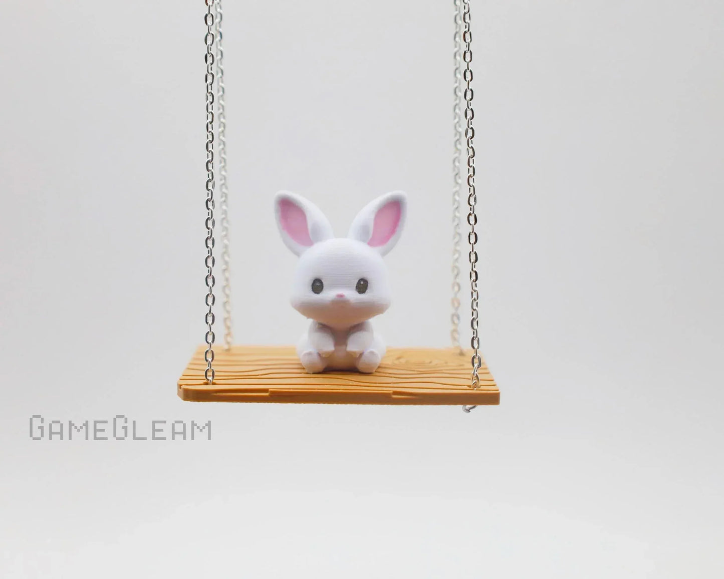 Cute white bunny figurine with pink ears sitting on a small wooden swing with chain ropes