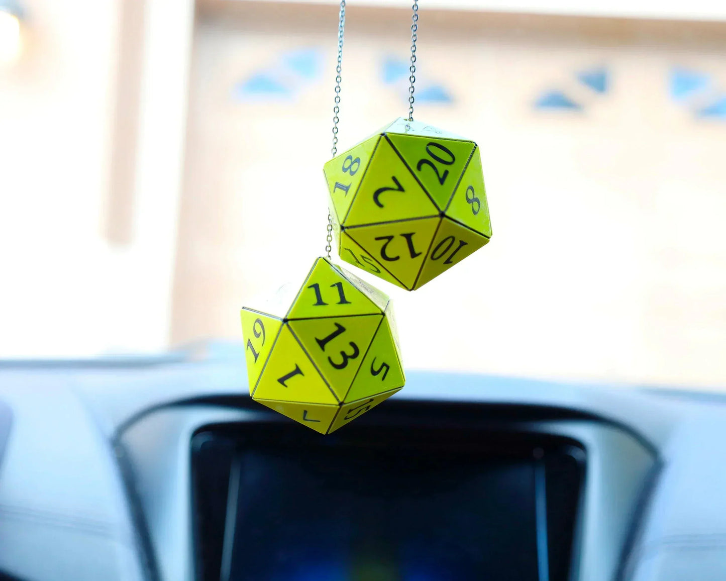 Yellow twenty-sided dice car charm hanging from rearview mirror in a vehicle interior