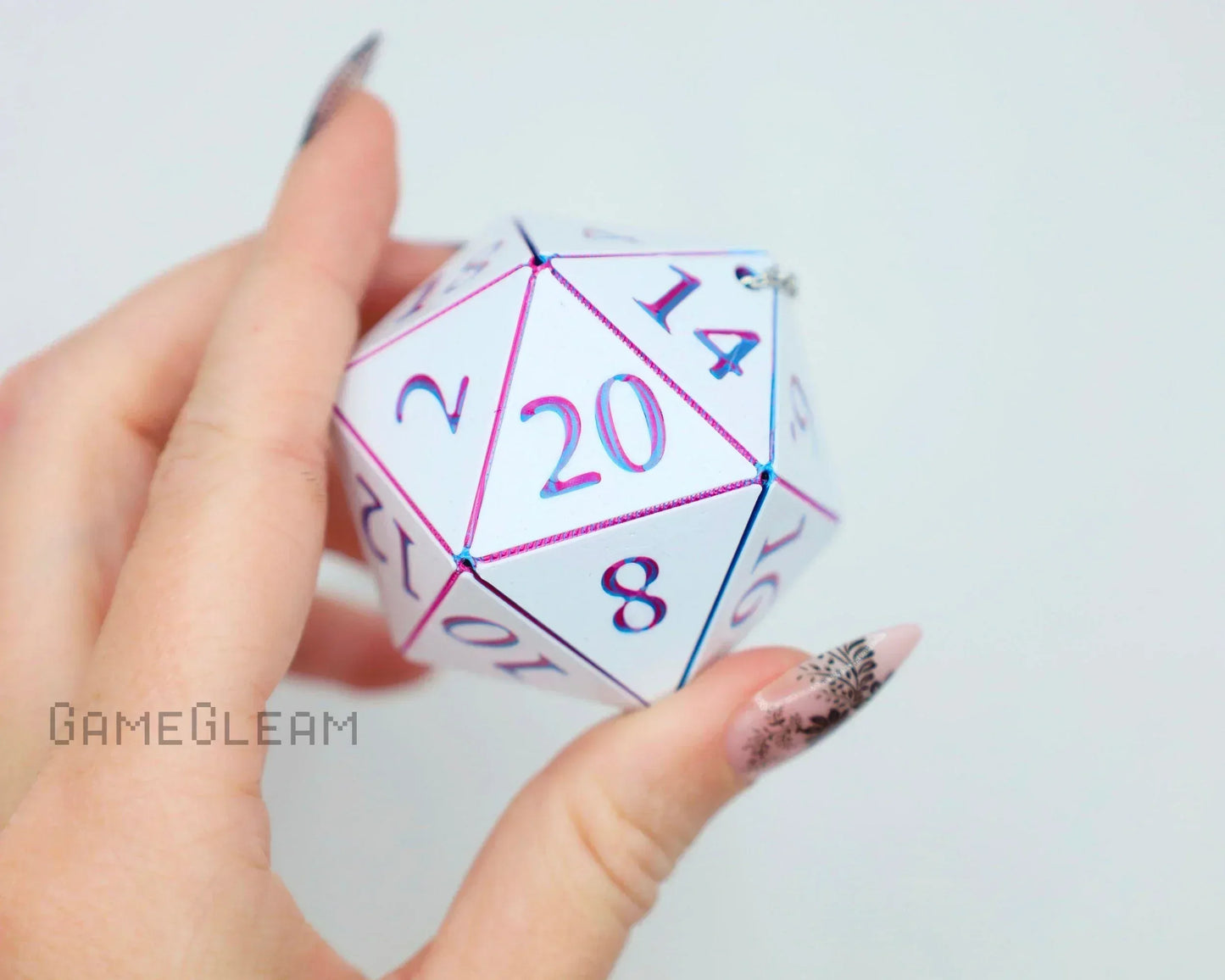 Hand holding a holographic white 20-sided dice charm with pink and blue numbers.