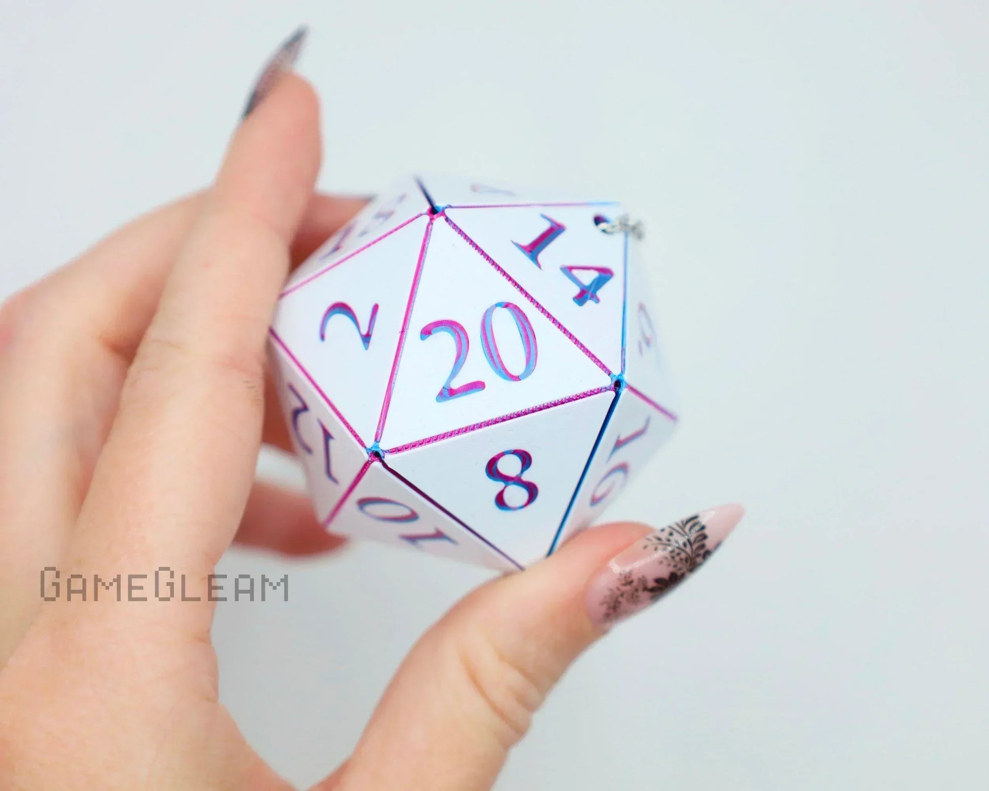 Hand holding a holographic white 20-sided dice charm with pink and blue numbers.