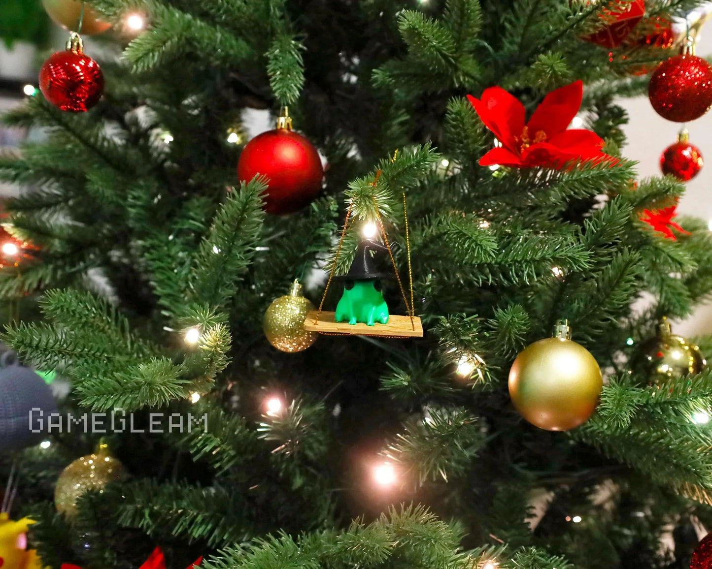 Christmas tree with red and gold ornaments and a green frog witch ornament on a swing.