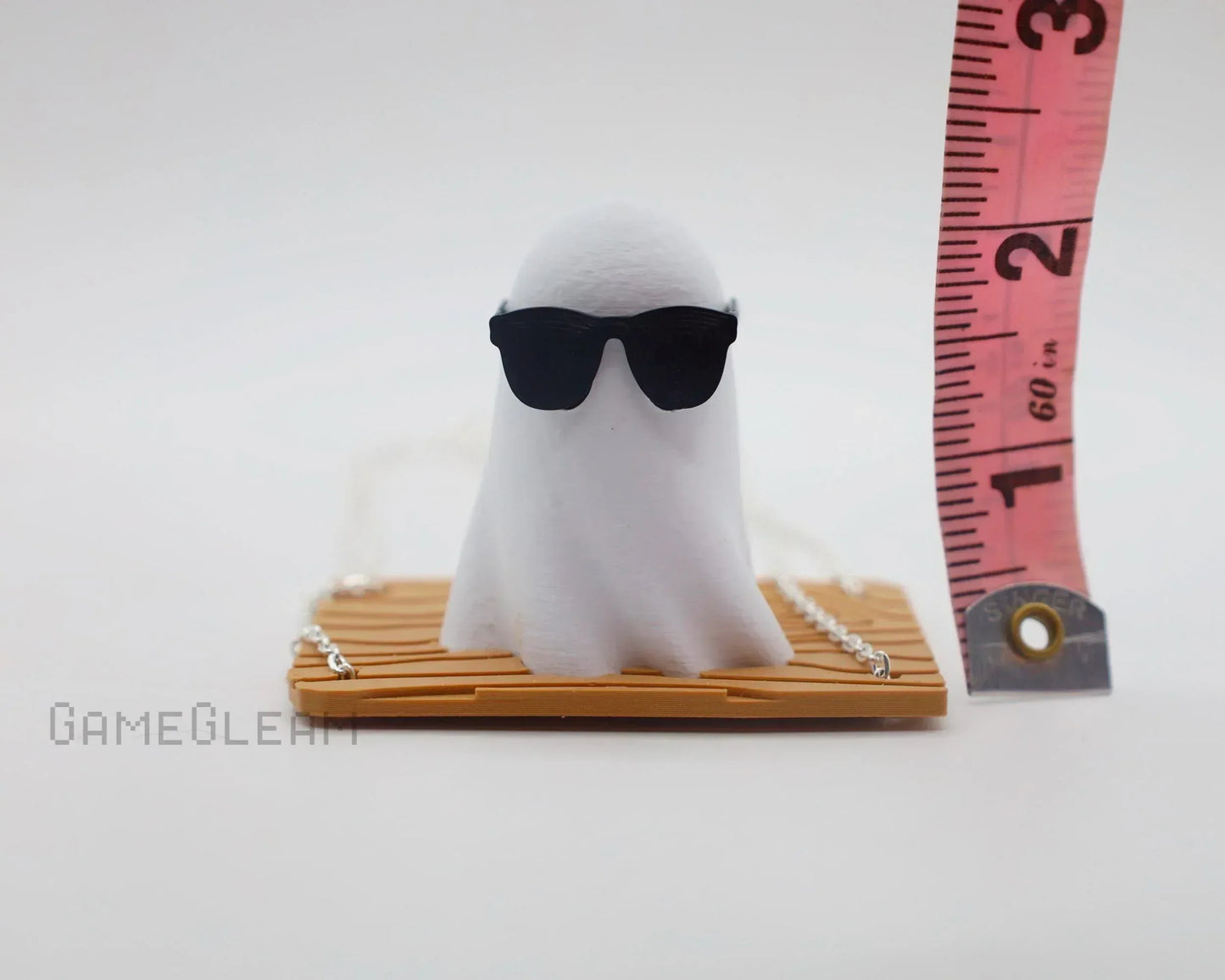 Handmade ghost figurine with sunglasses on wooden base next to measuring tape