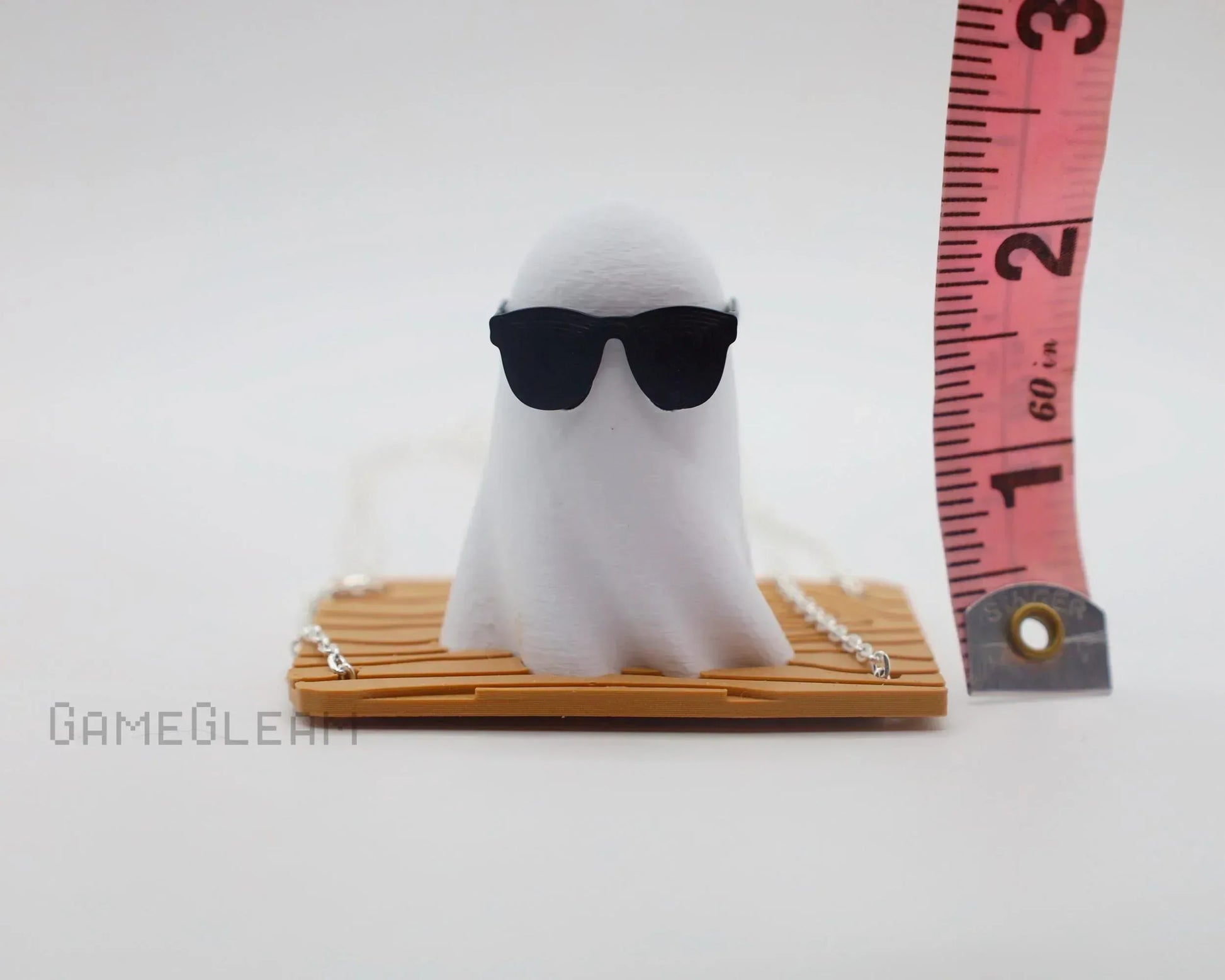 Handmade ghost figurine with sunglasses on wooden base next to measuring tape