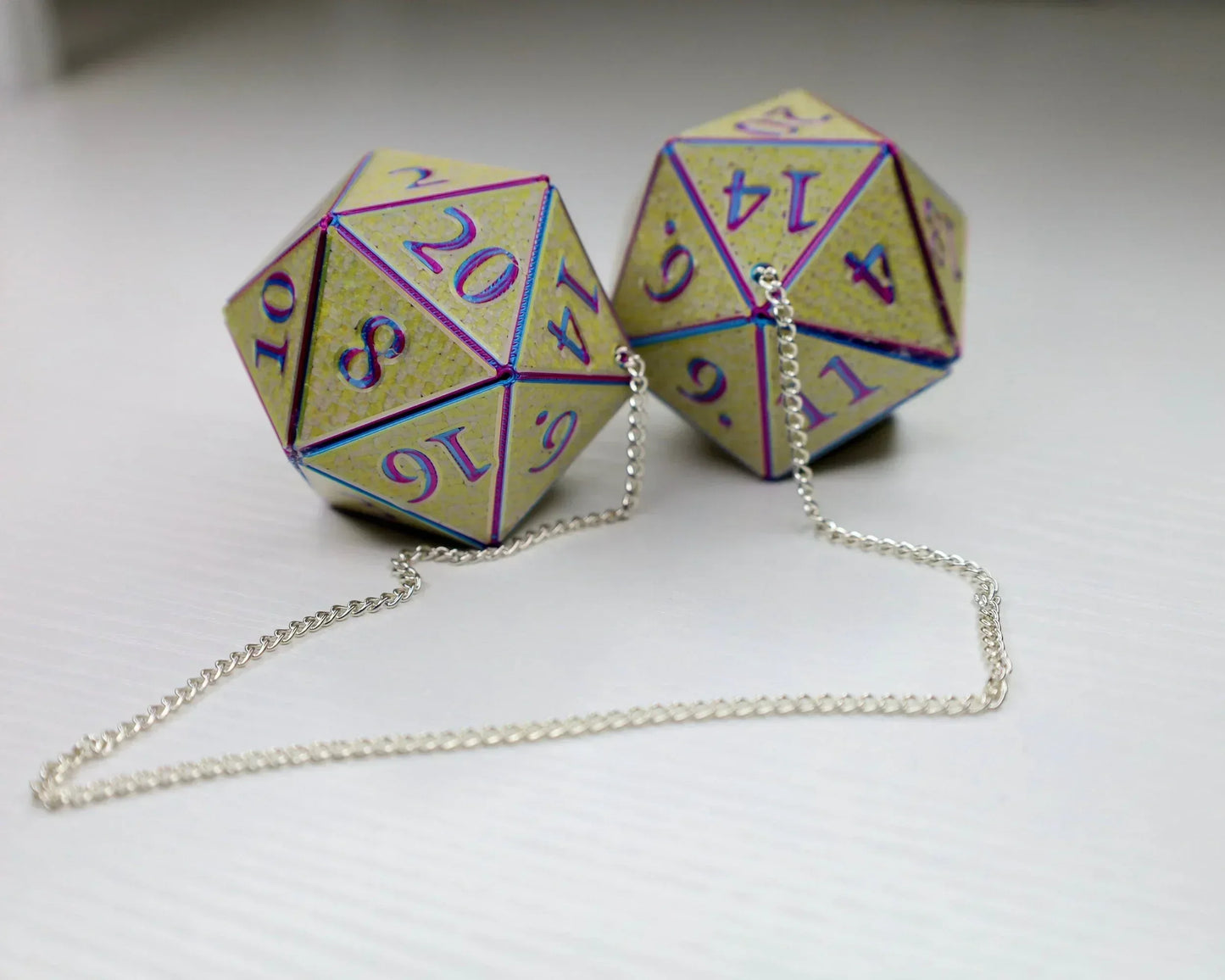 Holographic yellow twenty-sided dice car charm connected by silver chain on white surface