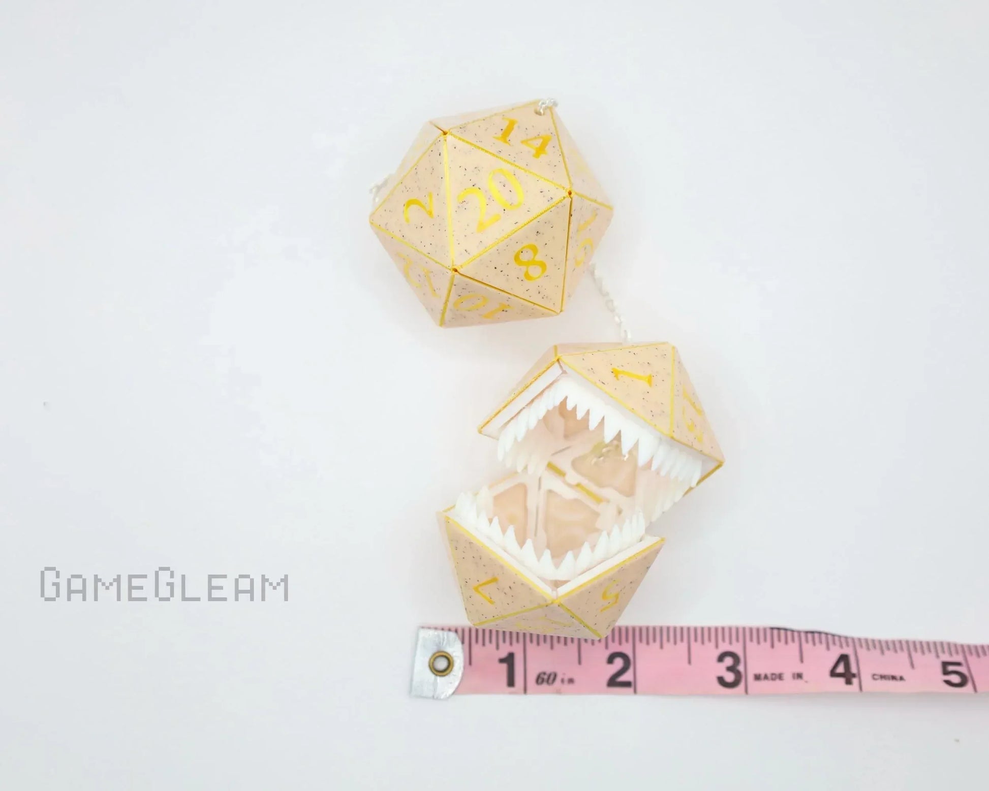 Handmade gold twenty-sided dice charm with teeth, next to measuring tape on white background