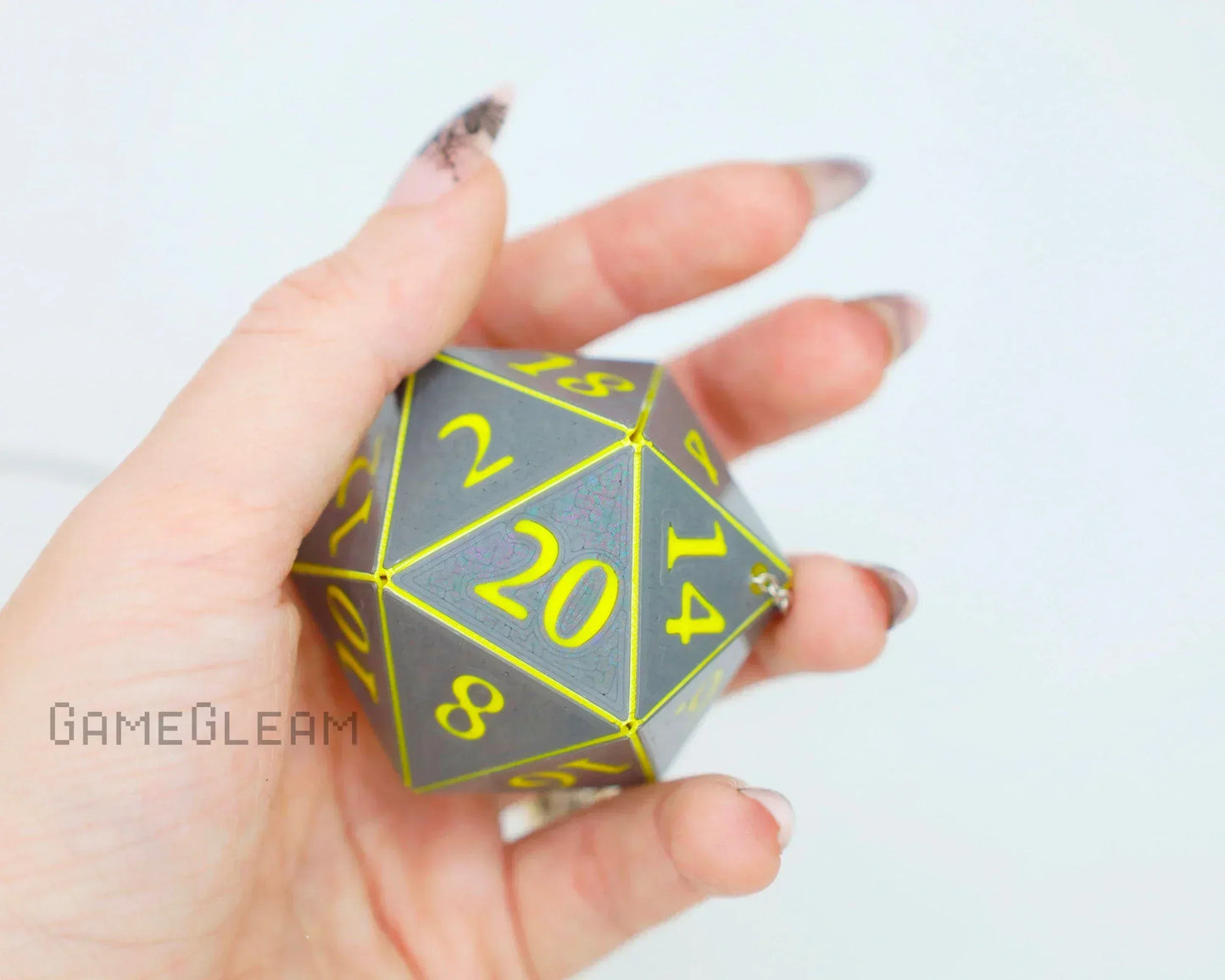 Hand holding a holographic gray twenty-sided dice charm with yellow numbers