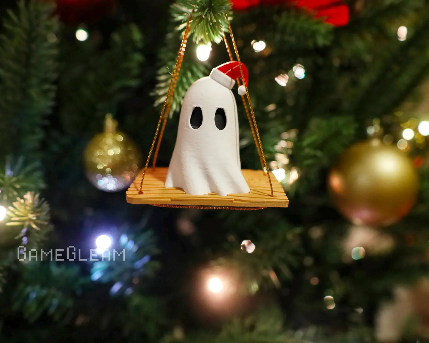 Handmade ghost ornament with Santa hat on swing, hanging on decorated Christmas tree