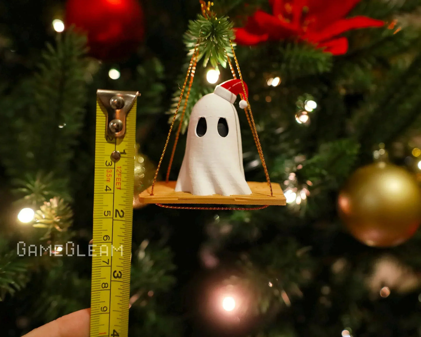 Handmade ghost ornament with Santa hat on a swing, measured by tape, hanging on Christmas tree