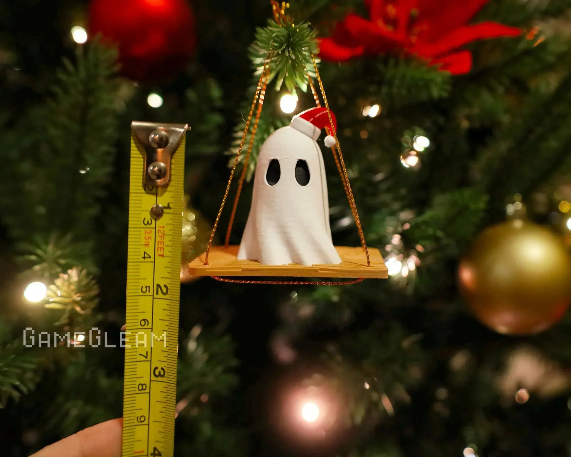 Handmade ghost ornament with Santa hat on a swing, measured by tape, hanging on Christmas tree