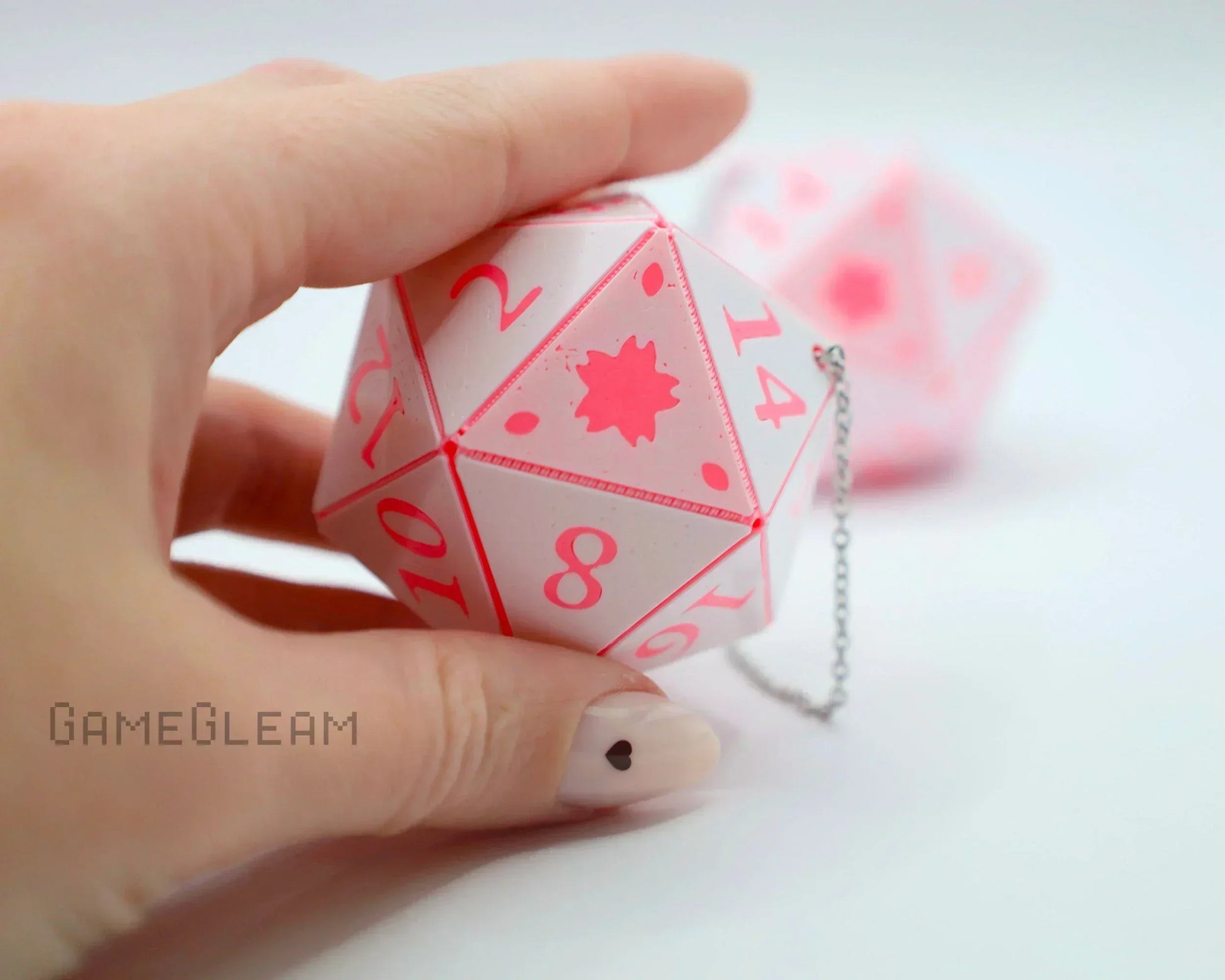 Hand holding a pink twenty-sided car dice charm with a silver chain on white background