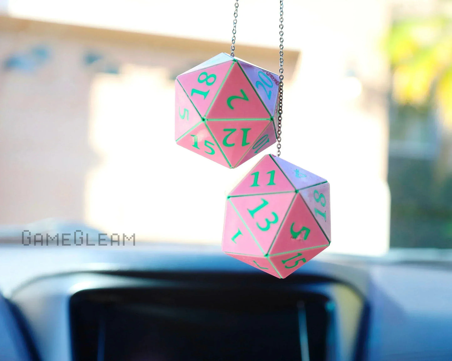 Pink twenty-sided dice car charm set with green numbers hanging from a rearview mirror.