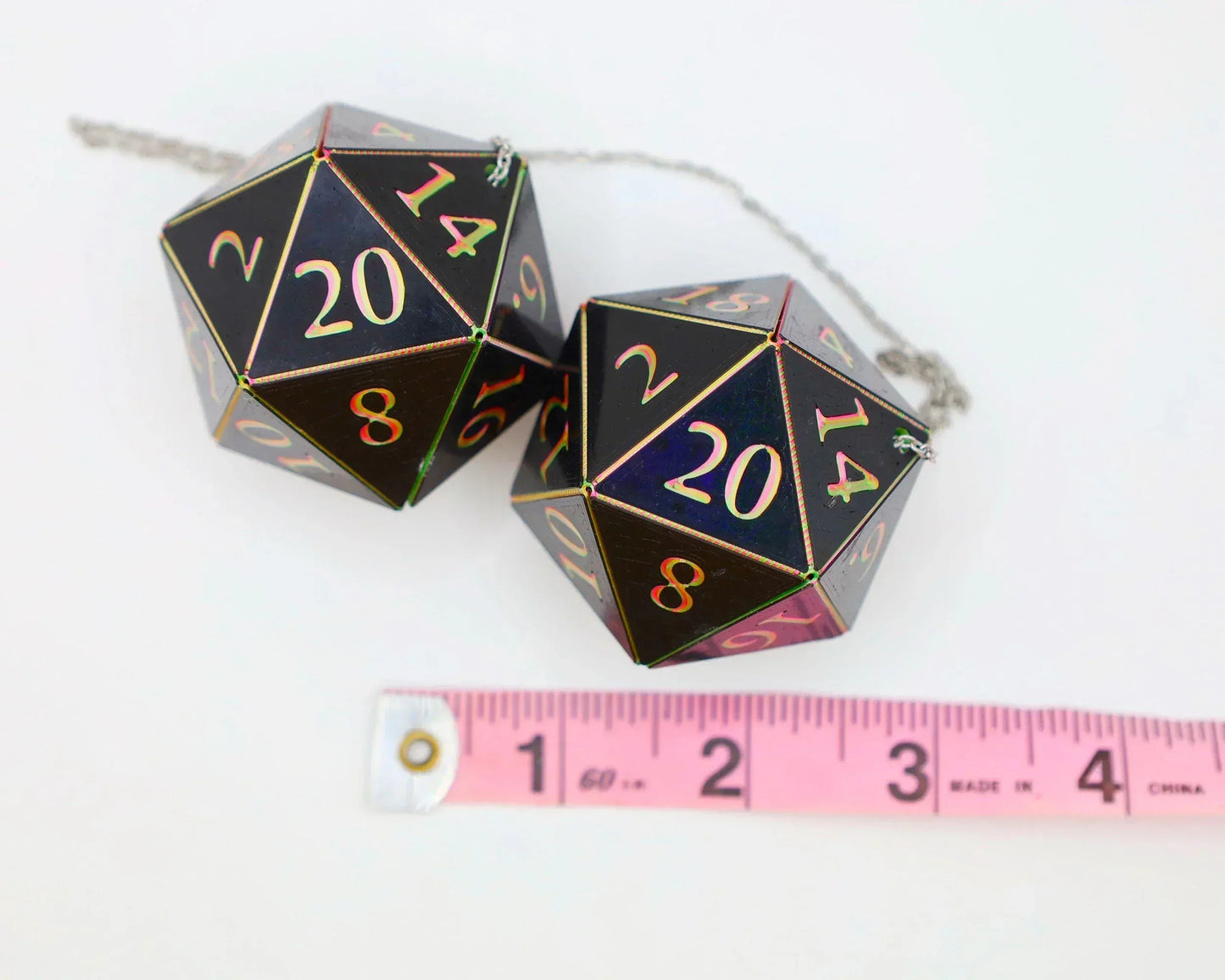 Holographic black twenty-sided dice car charms with chain, next to a pink measuring tape.