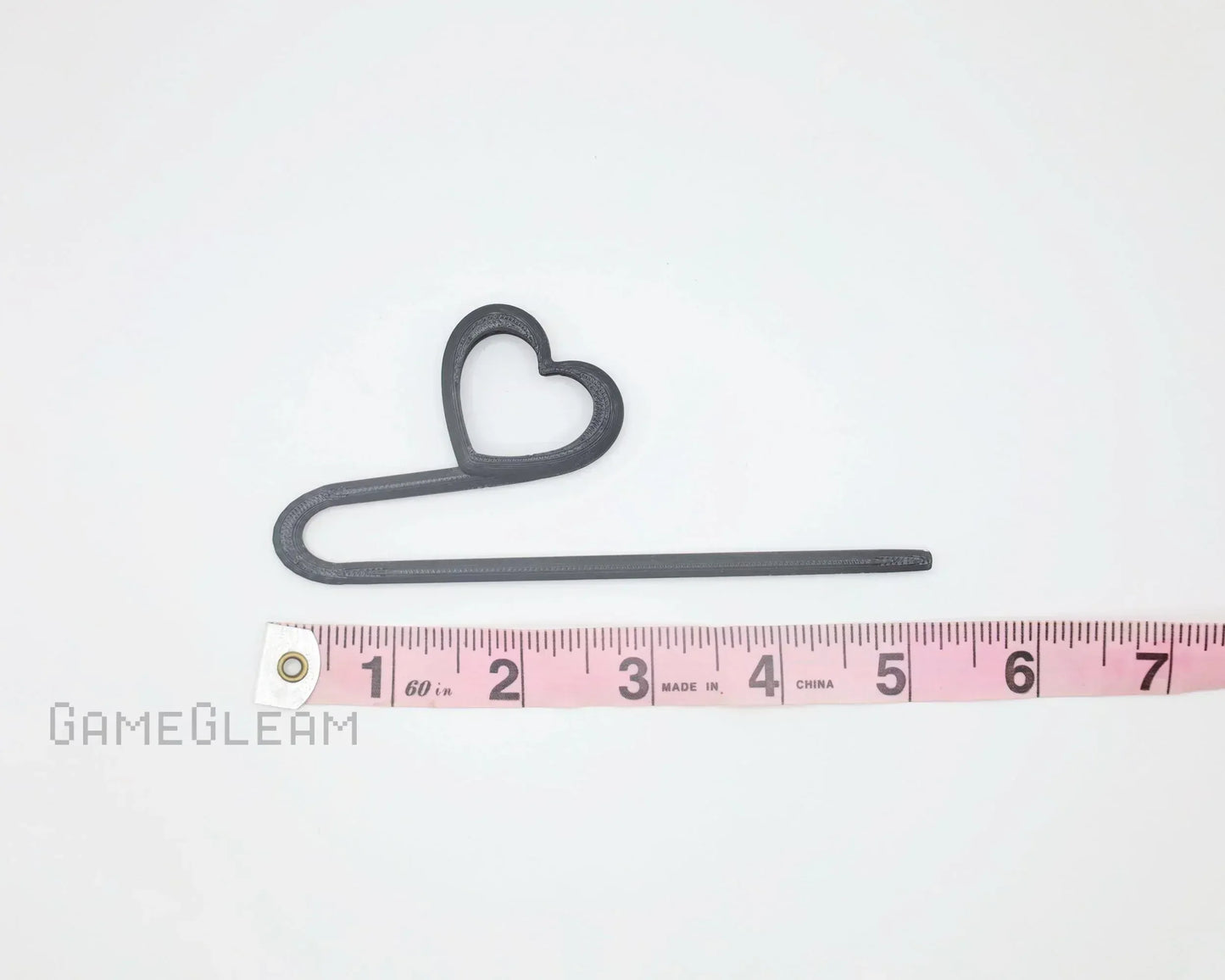 Black plastic heart-shaped stick accessory beside pink measuring tape on white background