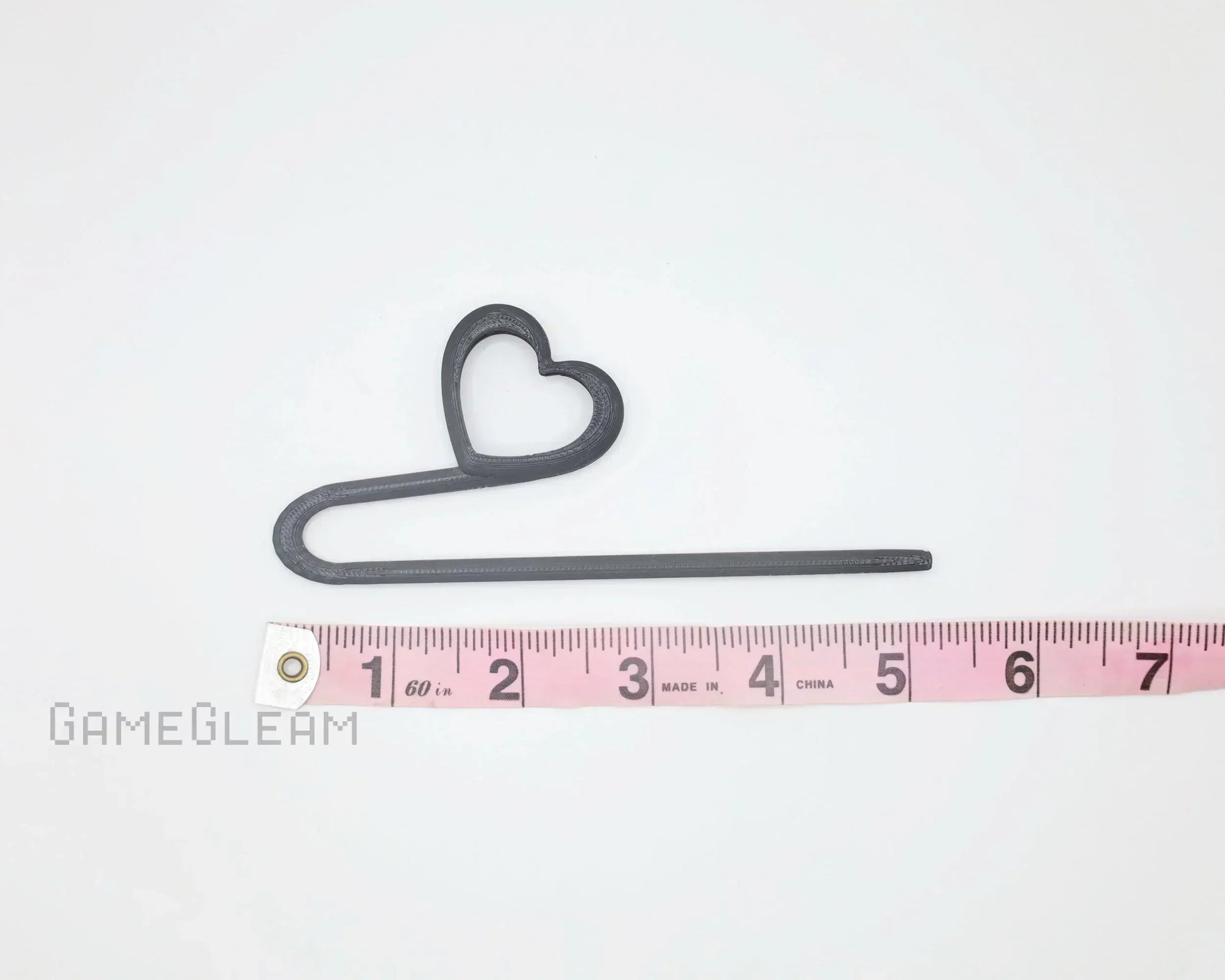 Black plastic heart-shaped stick accessory beside pink measuring tape on white background