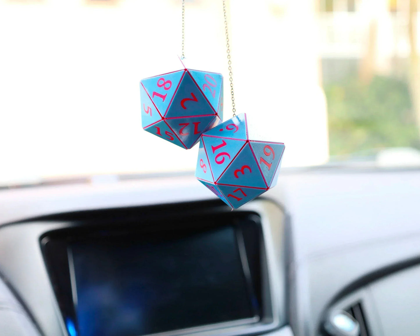 Blue and pink twenty-sided dice car charm hanging from a rearview mirror inside a car.