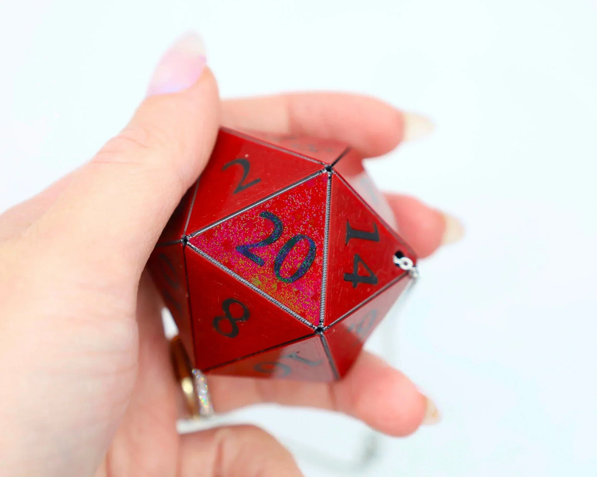 Hand holding a large red holographic 20-sided dice charm with black numbers.