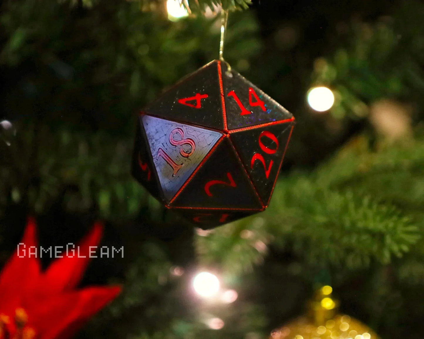 Holographic black and red twenty-sided dice ornament hanging on a Christmas tree branch