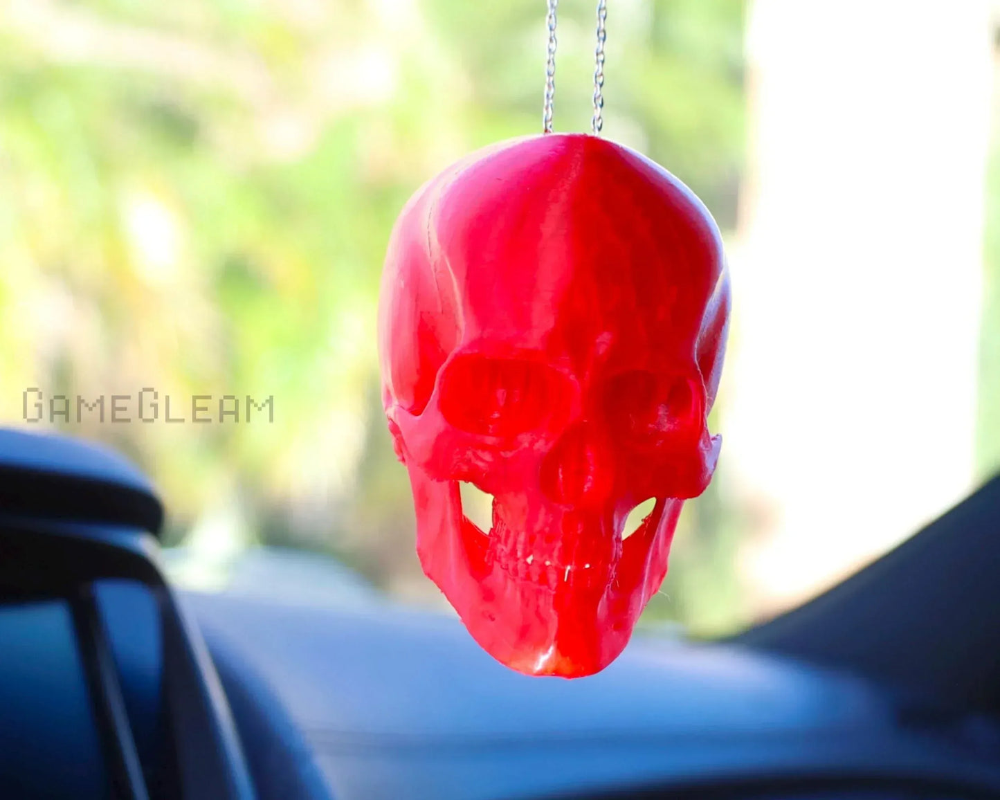 Red resin skull car charm hanging from a rearview mirror, handmade accessory.