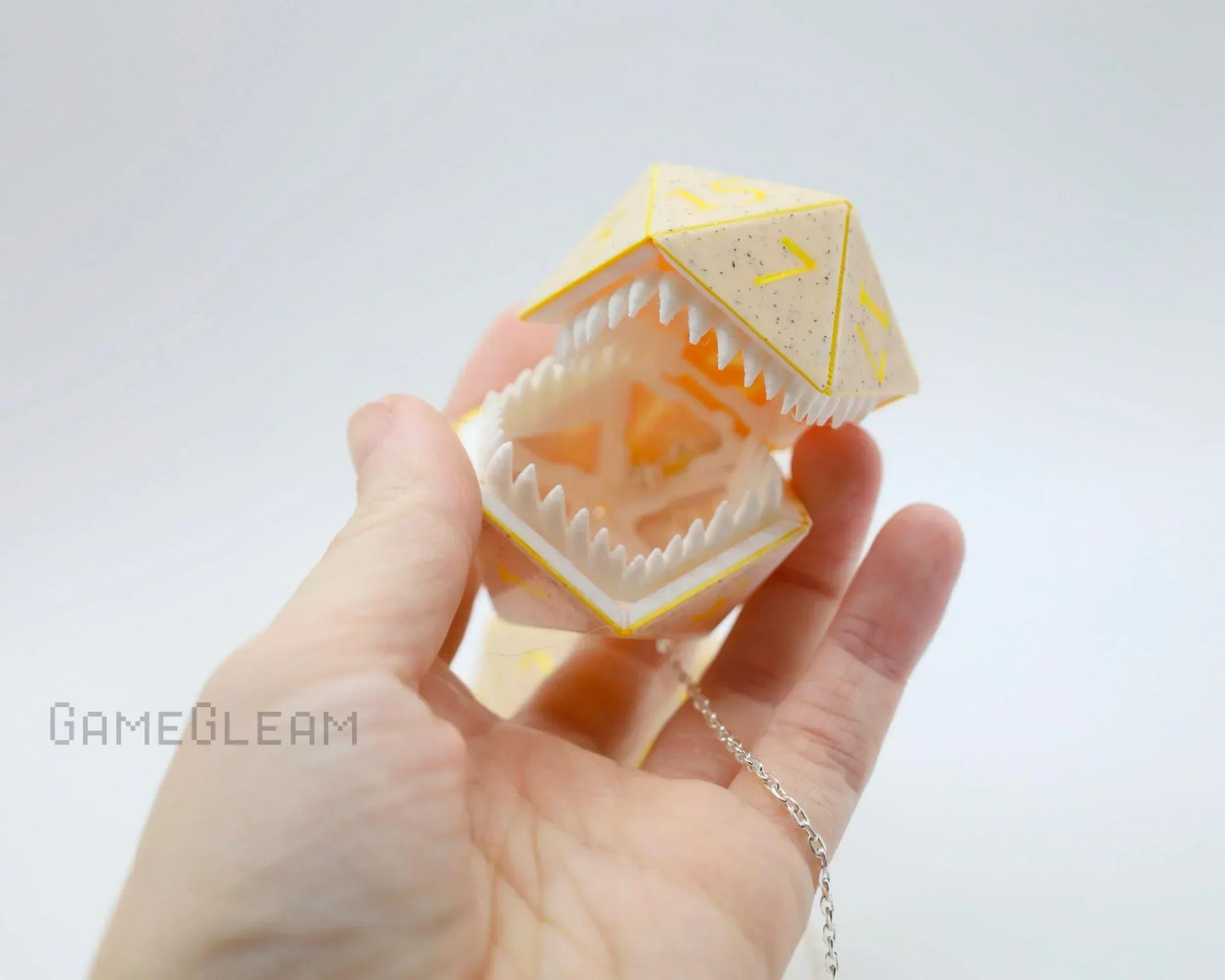 Hand holding yellow polyhedral dice charm with open mouth and pointed teeth, geek gamer gift.