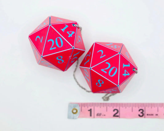 Pink 20-sided dice car charm with blue numbers, chain attached, next to measuring tape