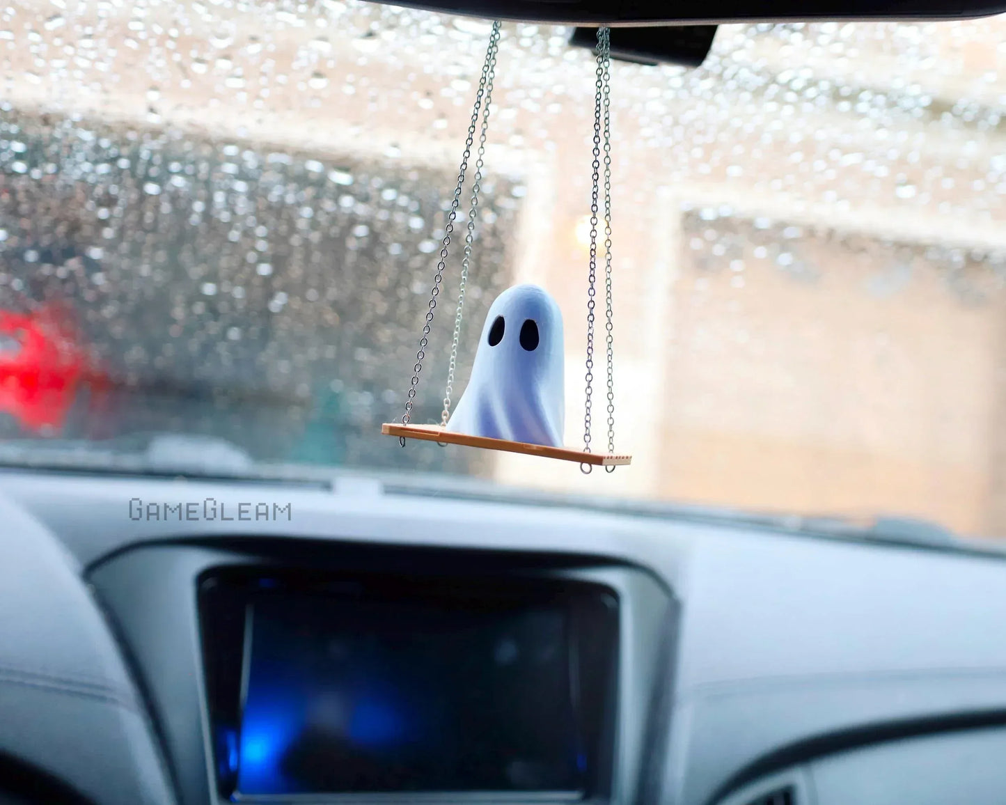 Handmade ghost car charm on swing, hanging from rearview mirror with raindrops on window