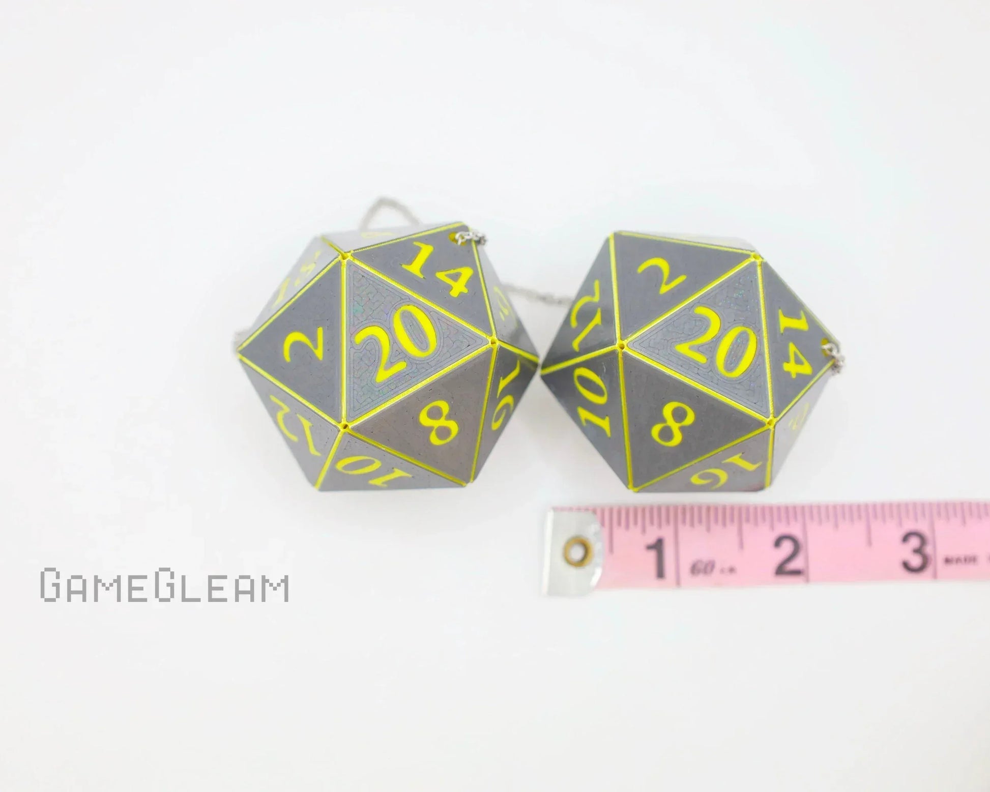 Pair of gray holographic 20-sided dice with yellow numbers and measuring tape for scale
